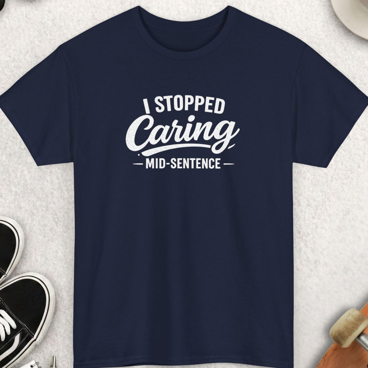 Navy blue t-shirt with 'I Stopped Caring Mid-Sentence' text on a light gray surface with accessories.