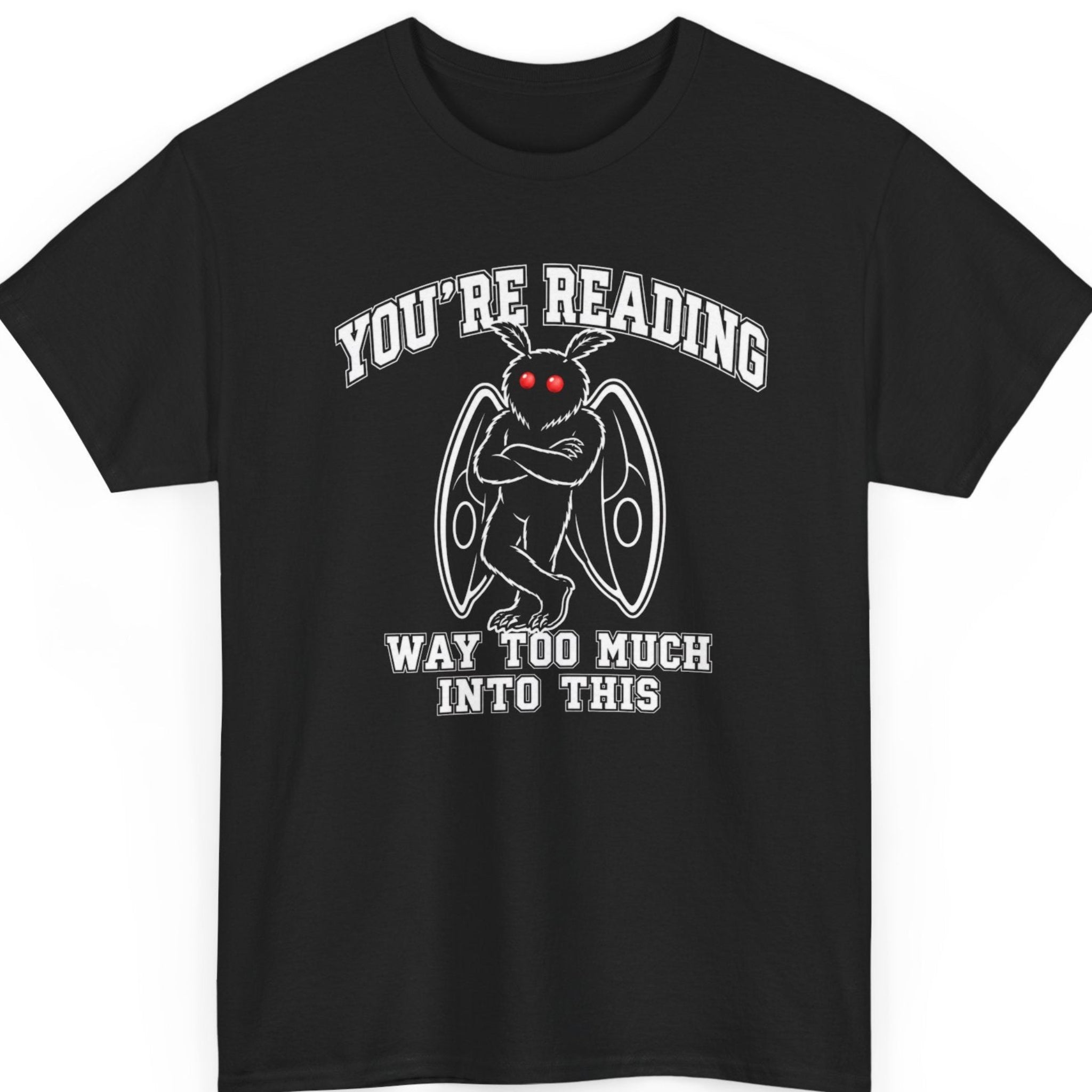 Mayhem Haus Mothman graphic t-shirt on a black shirt featuring a minimalist cartoon Mothman with glowing red eyes, folded wings, and crossed arms beneath bold varsity-style typography reading "YOU'RE READING WAY TOO MUCH INTO THIS."