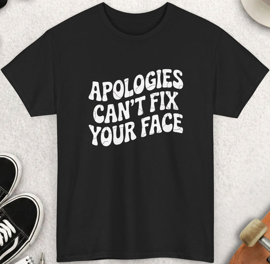 Black t-shirt with 'Apologies can't fix your face' text on a light gray surface with accessories.