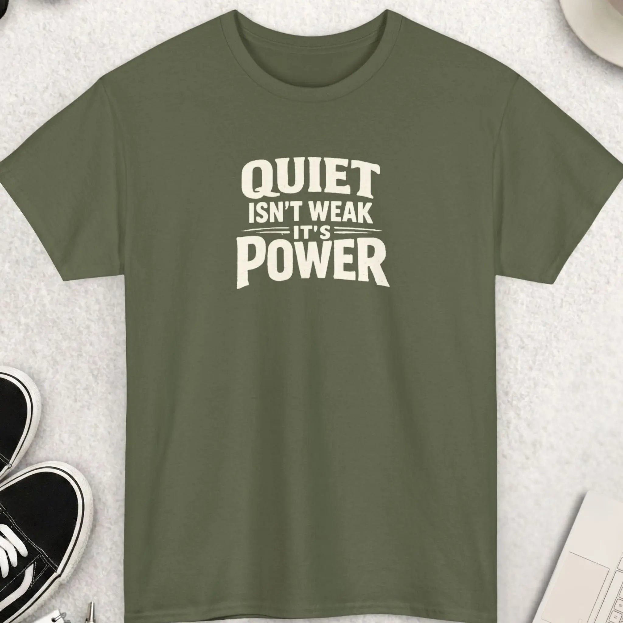 Military Green t-shirt with 'QUIET ISN'T WEAK IT'S POWER' text on a light gray surface with shoes, coffee, and accessories.