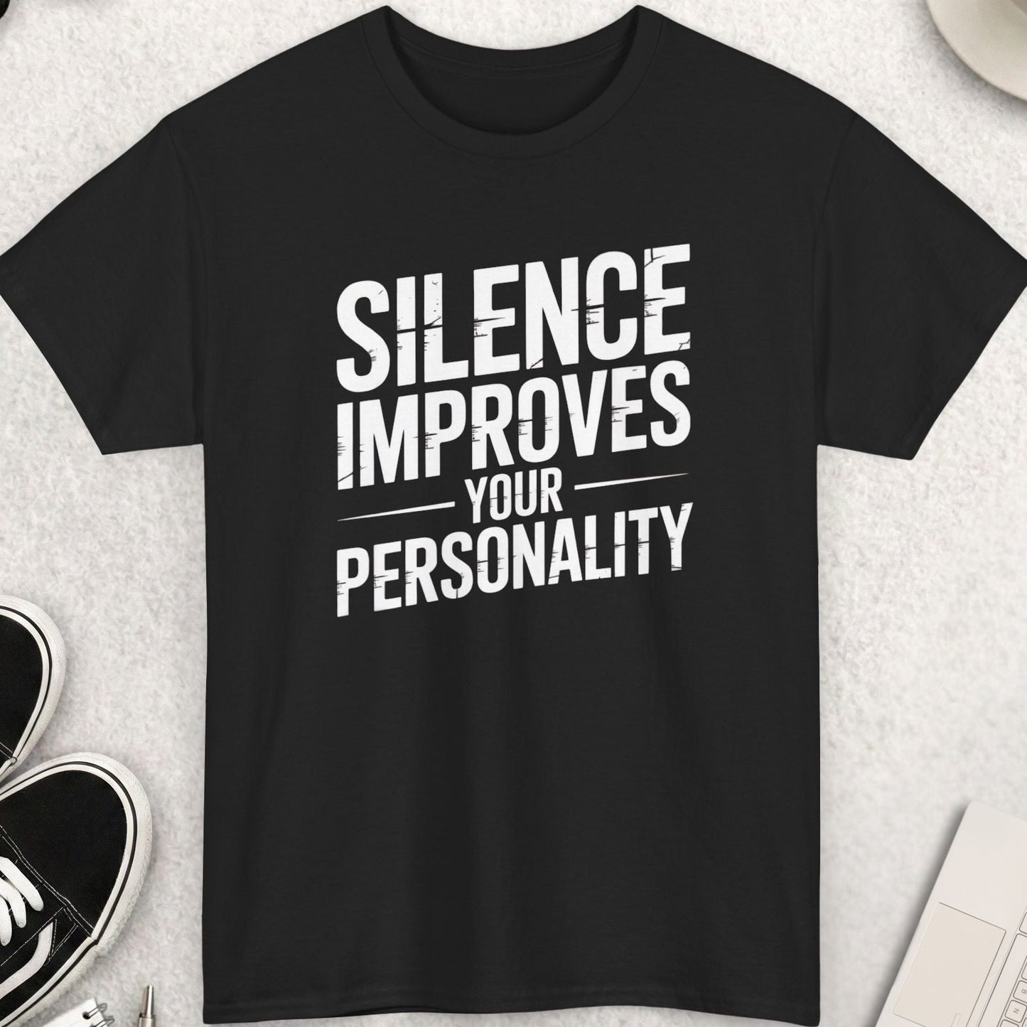 Black t-shirt with 'Silence Improves Your Personality' text on a light gray surface with shoes, coffee, and accessories.