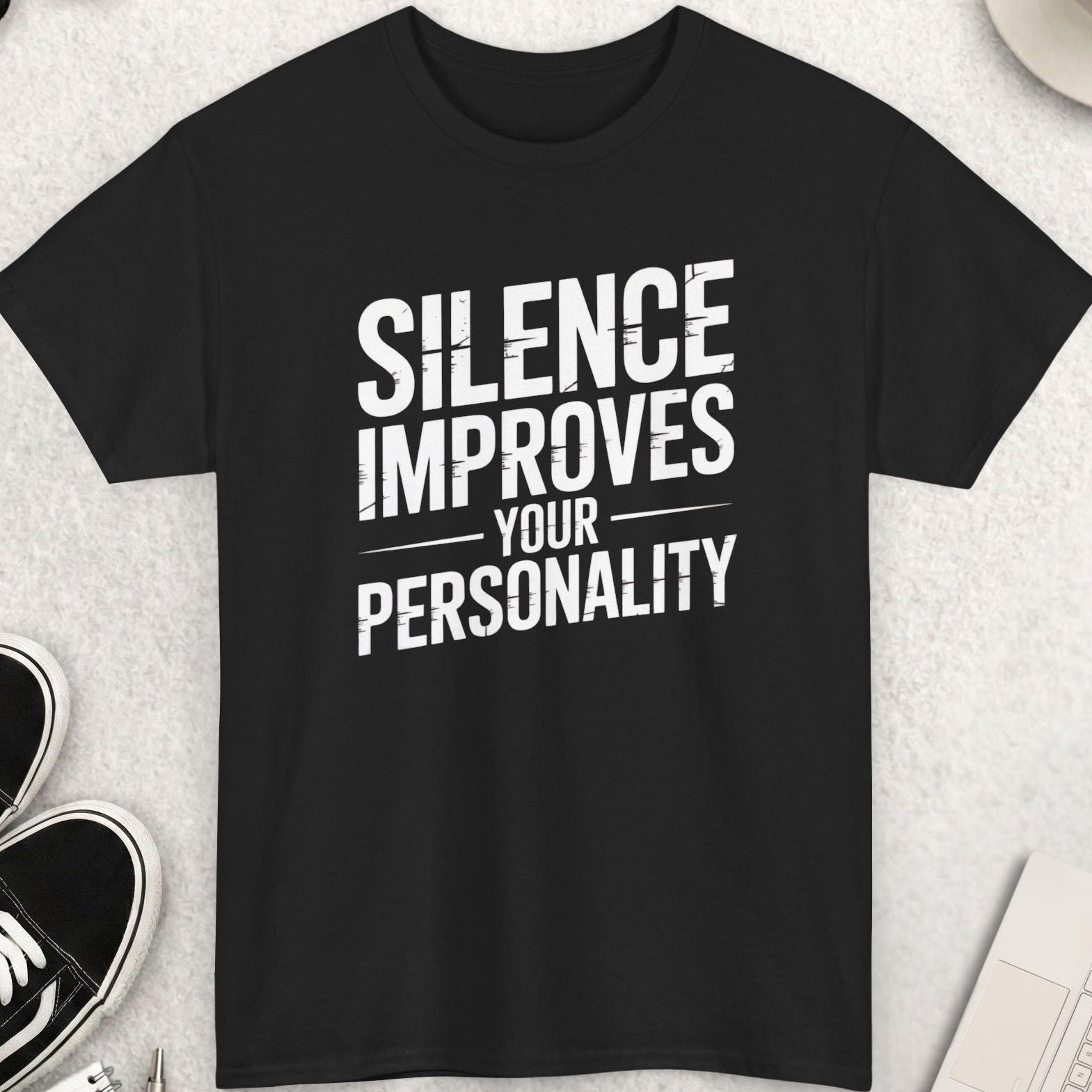 Black t-shirt with 'Silence Improves Your Personality' text on a light gray surface with shoes, coffee, and accessories.