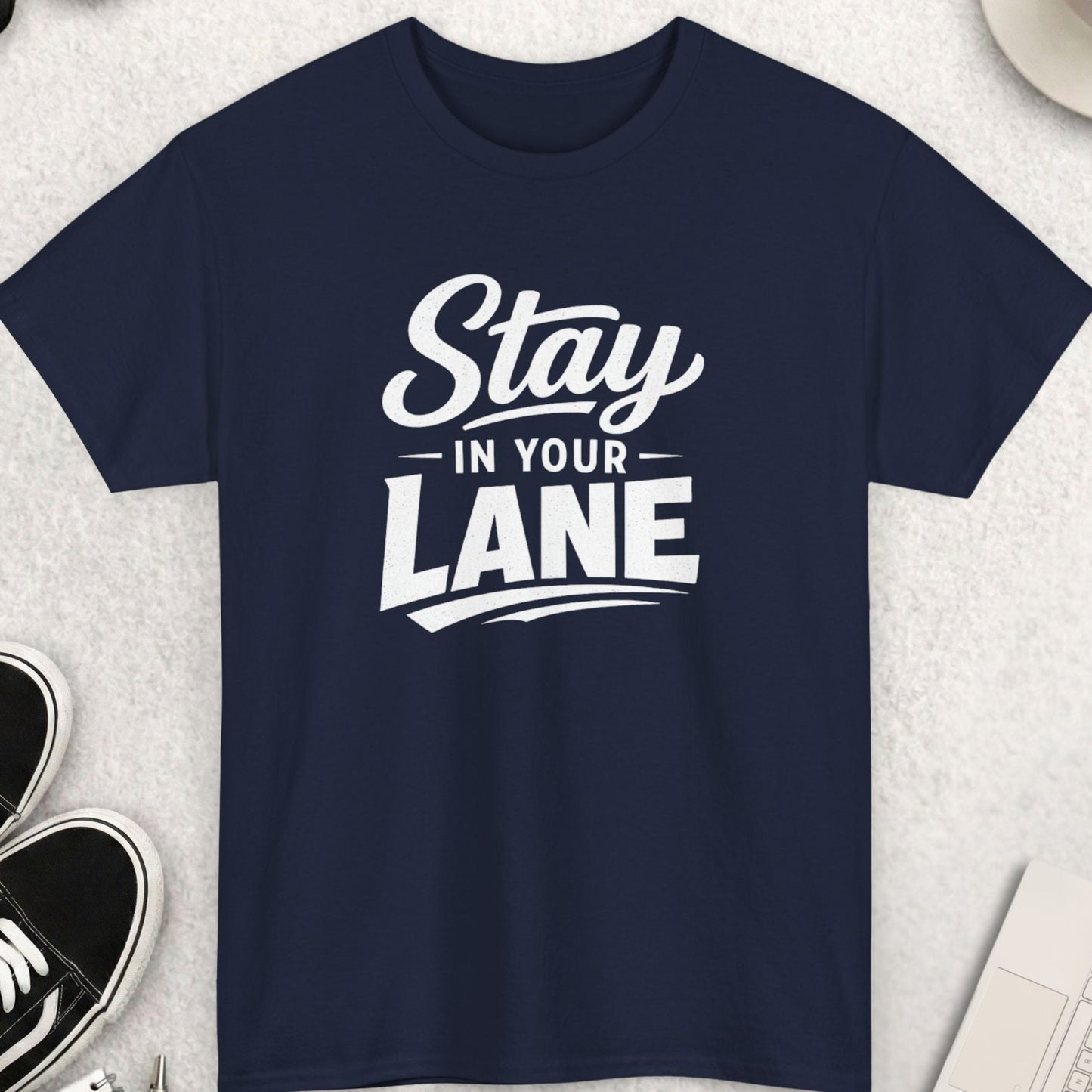 Navy blue t-shirt with 'Stay in Your Lane' text on a light gray surface with accessories.