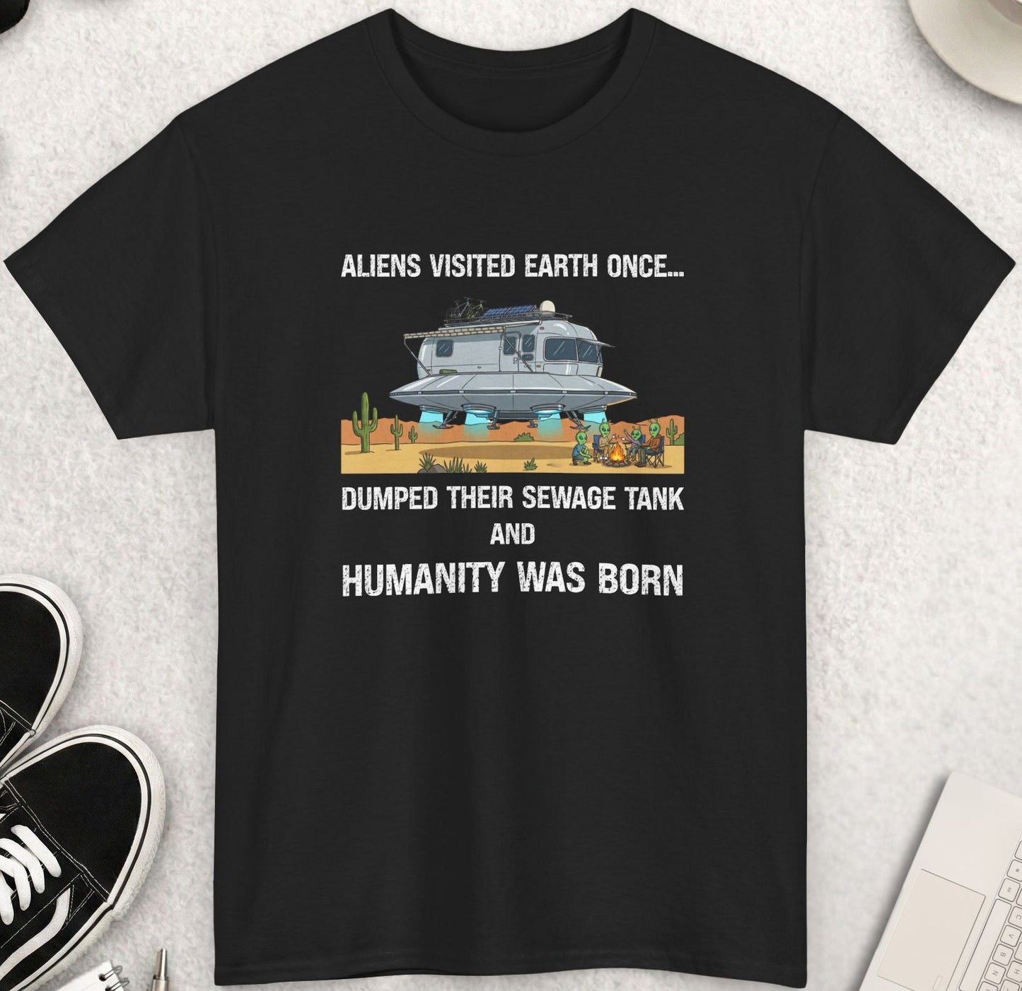 Black t-shirt with humorous graphic and text on a light gray surface with accessories.