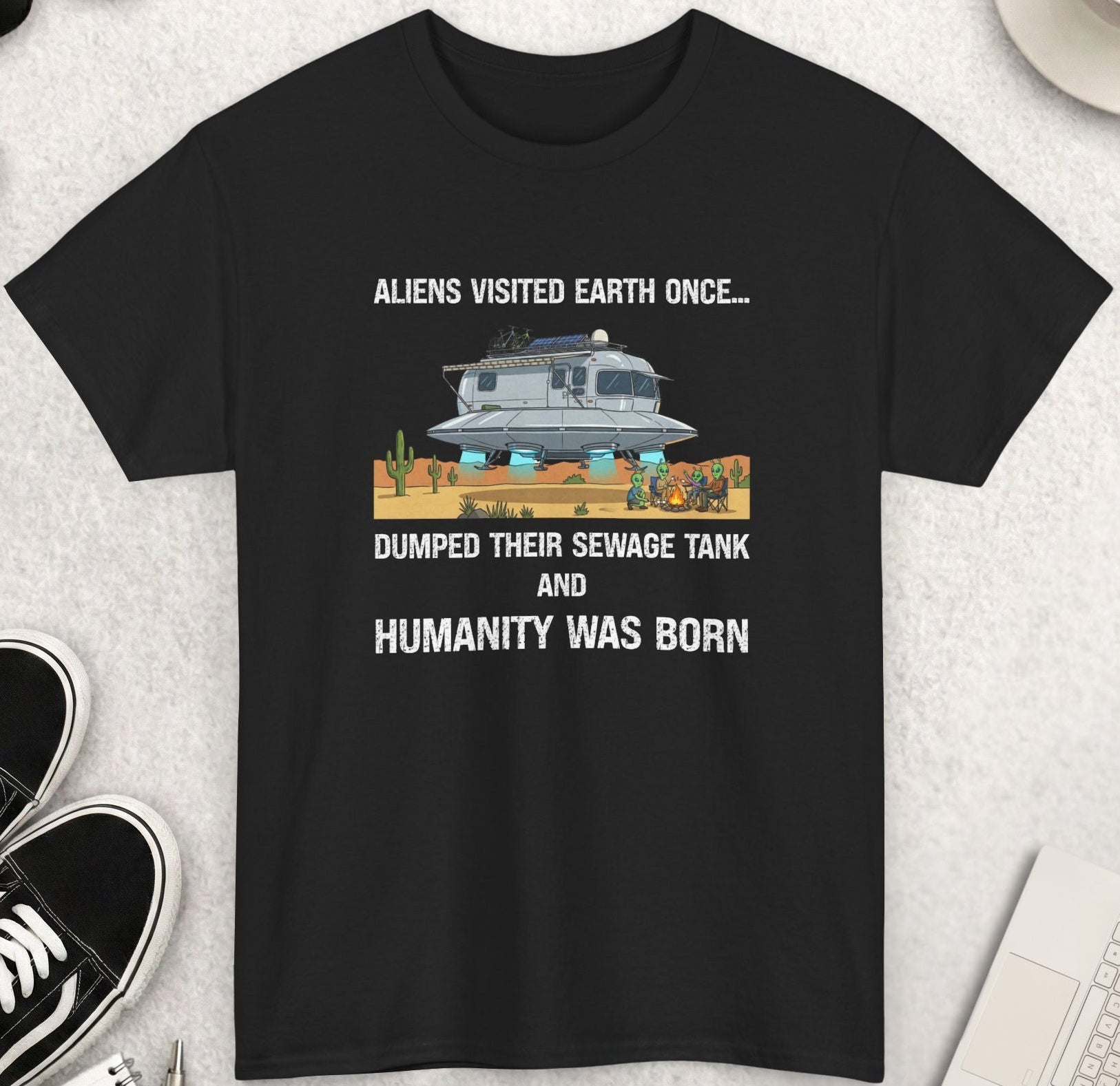 Black t-shirt with humorous graphic and text on a light gray surface with accessories.