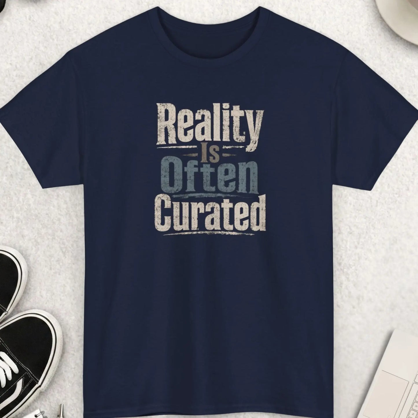 Reality Is Often Curated vintage distressed graphic t-shirt featuring aged cream, muted gray, and faded blue typography on a navy blue shirt with rugged worn print texture and thought-provoking message.