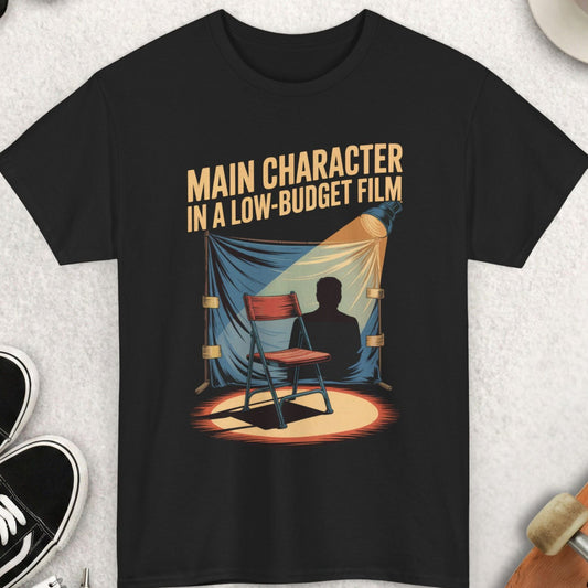 Black t-shirt with graphic design and text on a light gray surface with accessories.