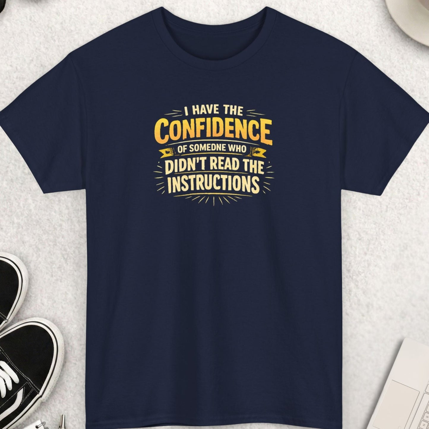 Navy blue t-shirt with humorous text design on a light gray surface with accessories.