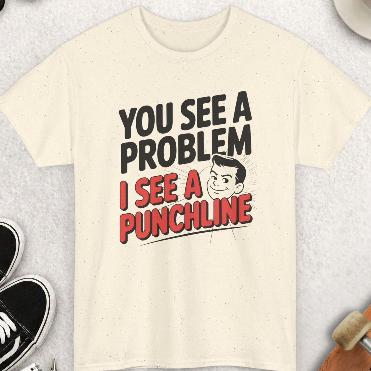 Beige t-shirt with humorous text design on a gray surface with casual items around.