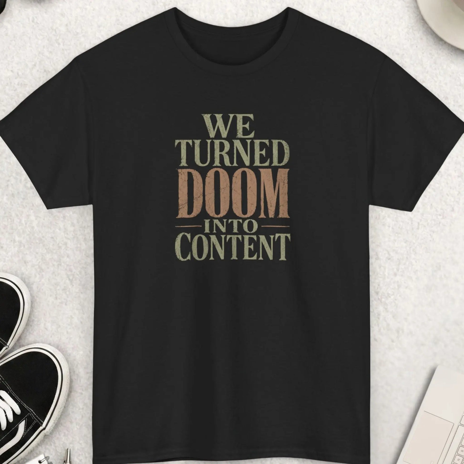 Distressed oversized serif typography t-shirt reading “We Turned Doom Into Content” in muted cream and faded clay colors on a black shirt with dark humor streetwear aesthetic.