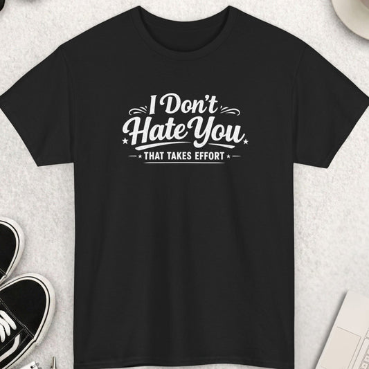 Black t-shirt with 'I Don't Hate You, That Takes Effort' text on a light gray surface with shoes, coffee, and accessories.
