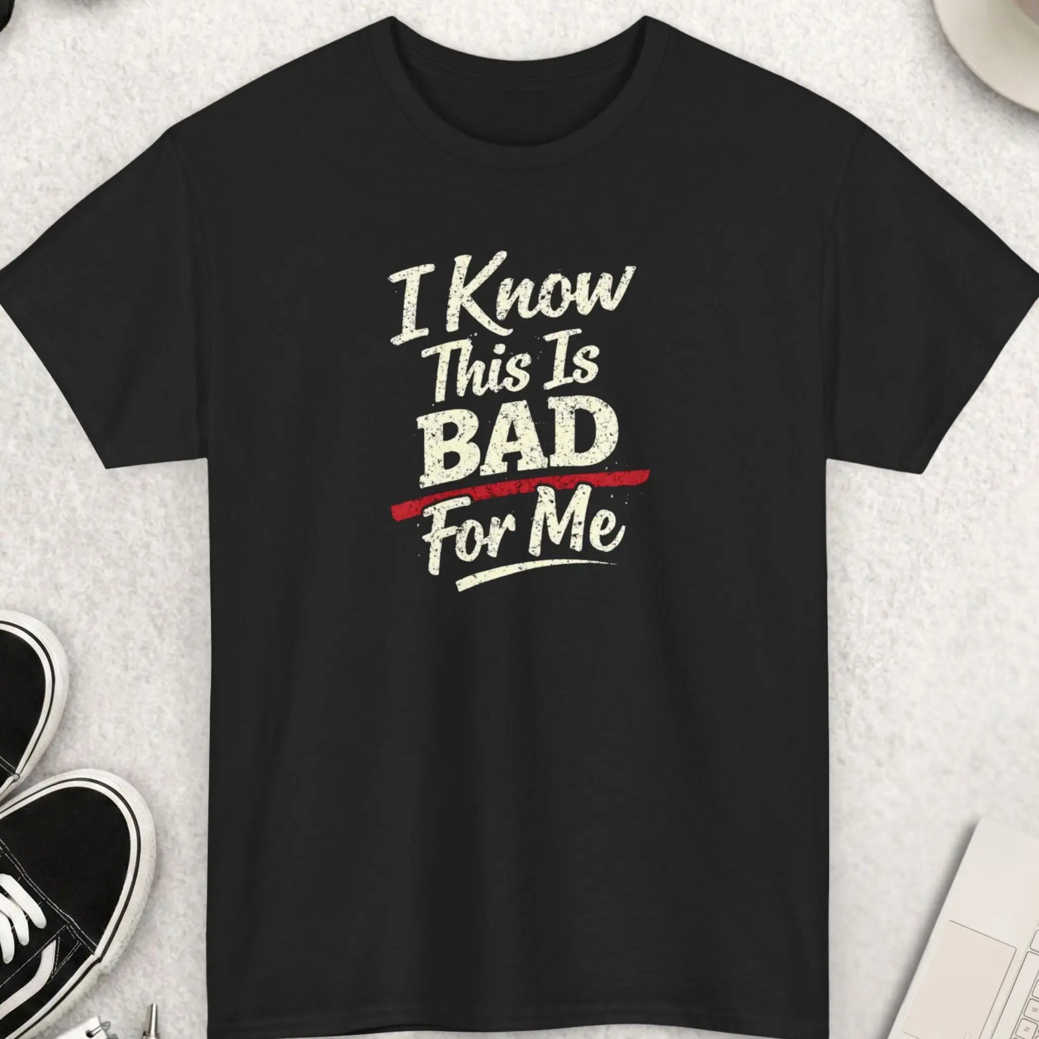 Black t-shirt with humorous text on a light gray surface with accessories.