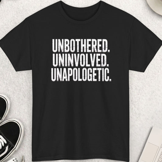 Black t-shirt with 'UNBOtherED. UNINvolved. UNApoLOGetic.' text on a light gray surface with shoes, coffee, and accessories.