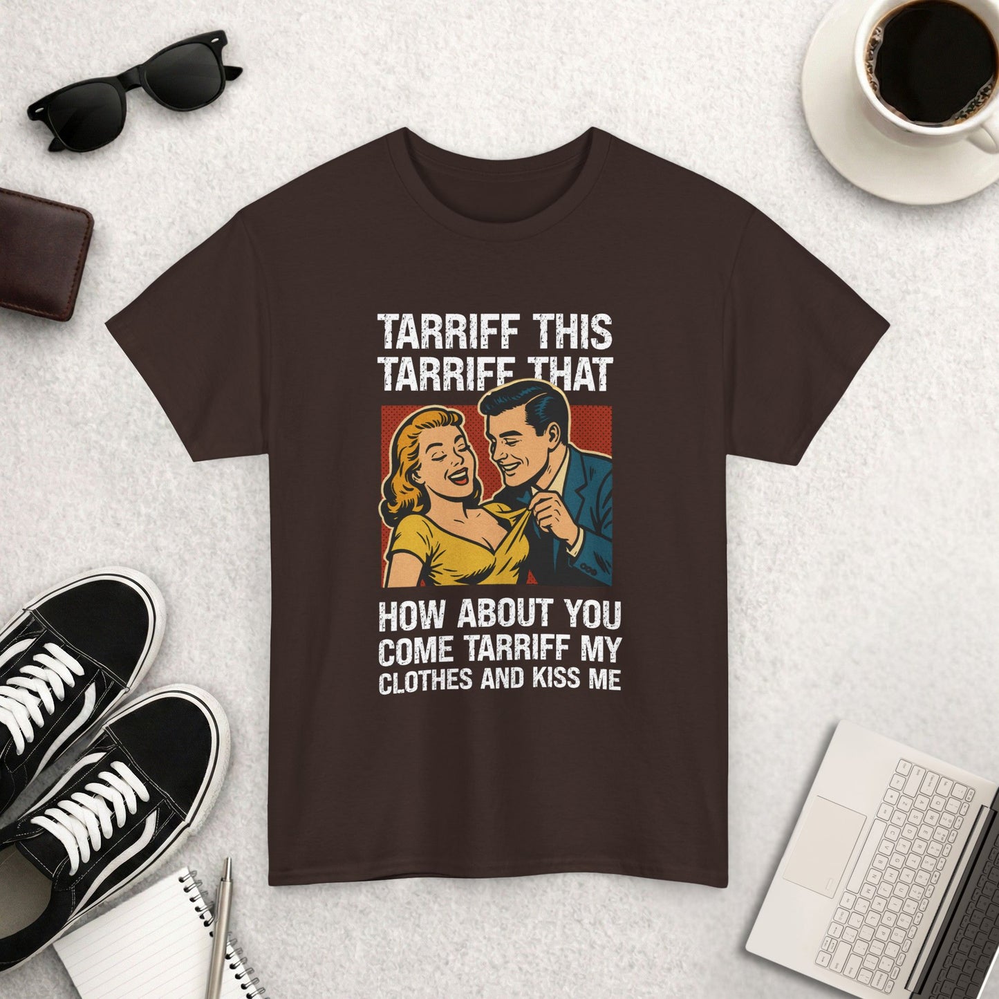 Brown t-shirt with graphic design and text on a light gray surface with accessories.