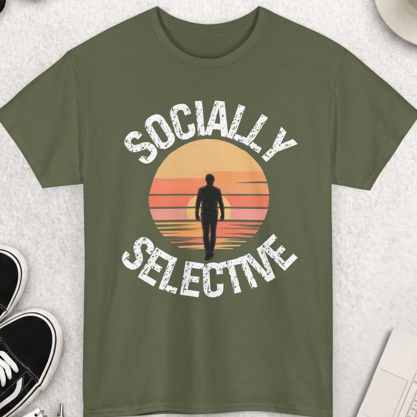 Green t-shirt with 'Socially Selective' design on a light gray surface with accessories.