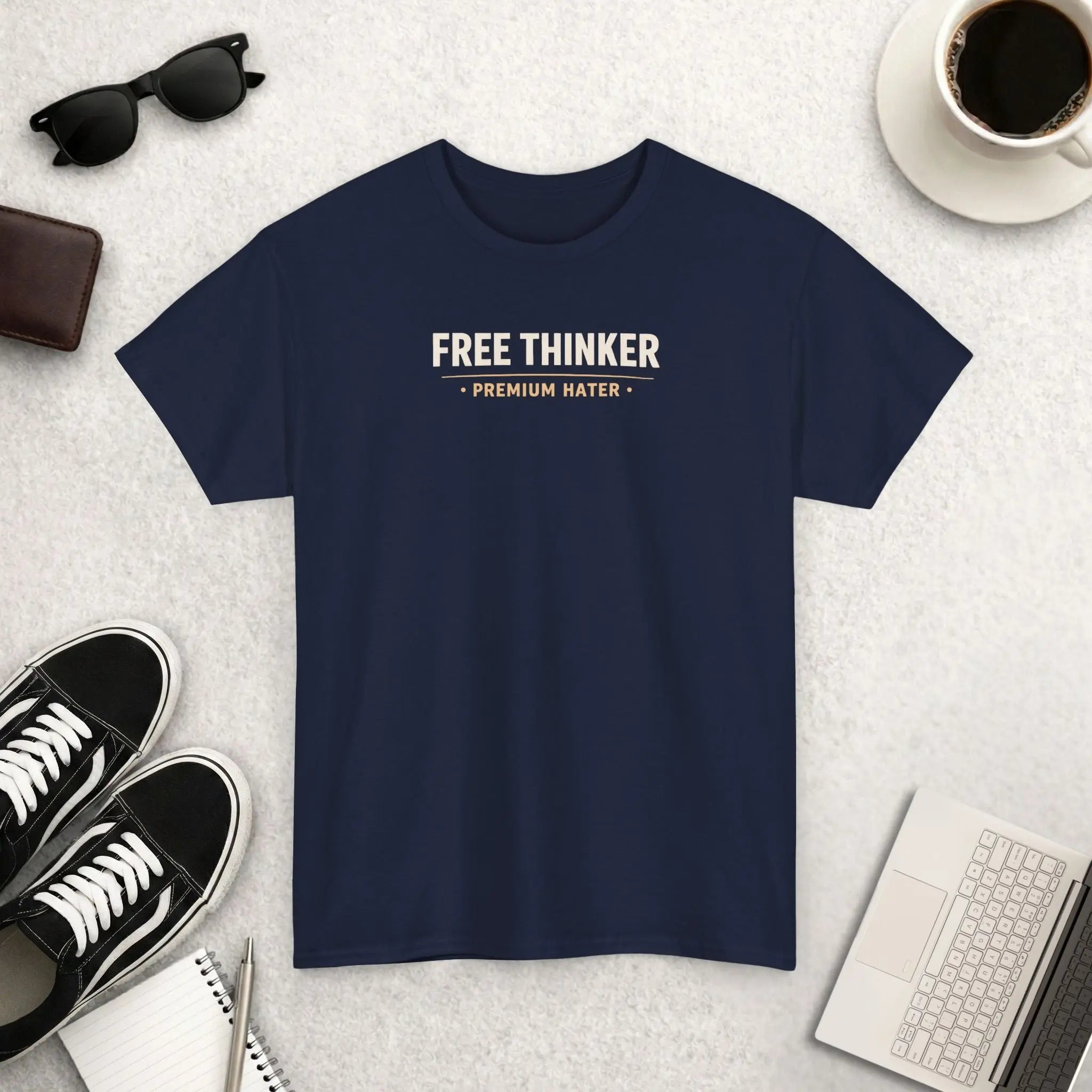 Navy blue t-shirt with 'Free Thinker Premium Hater' text on a light gray surface with accessories.