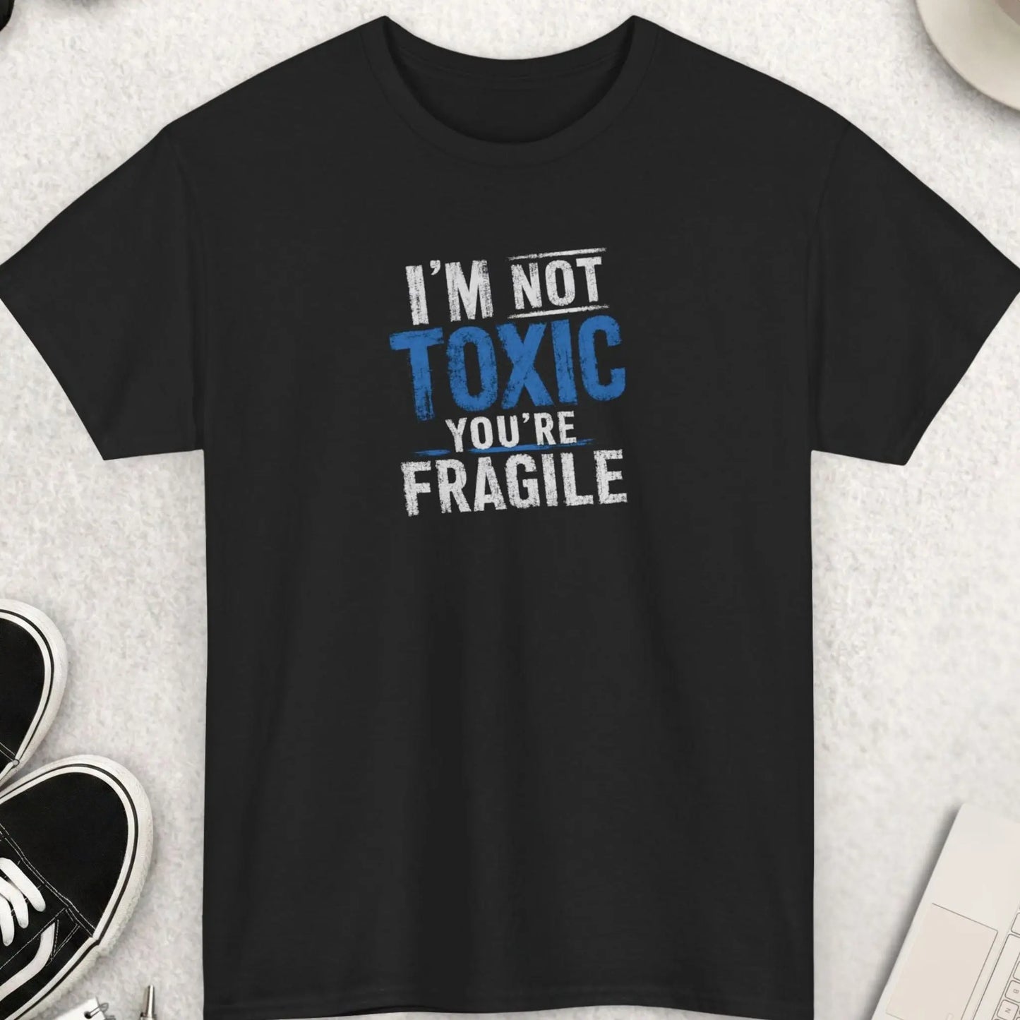 Black graphic t-shirt featuring distressed blue and white typography reading “I’m Not Toxic, You’re Fragile” in a bold sarcastic streetwear design.