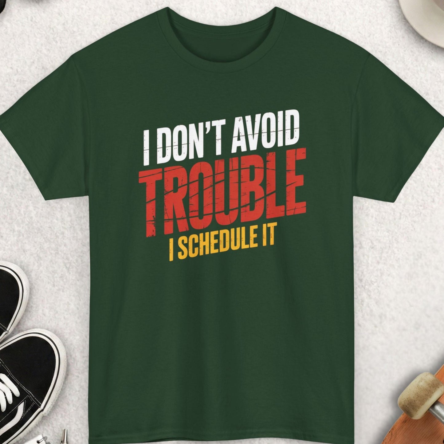 Green t-shirt with text 'I don't avoid trouble, I schedule it' on a light gray surface with accessories.