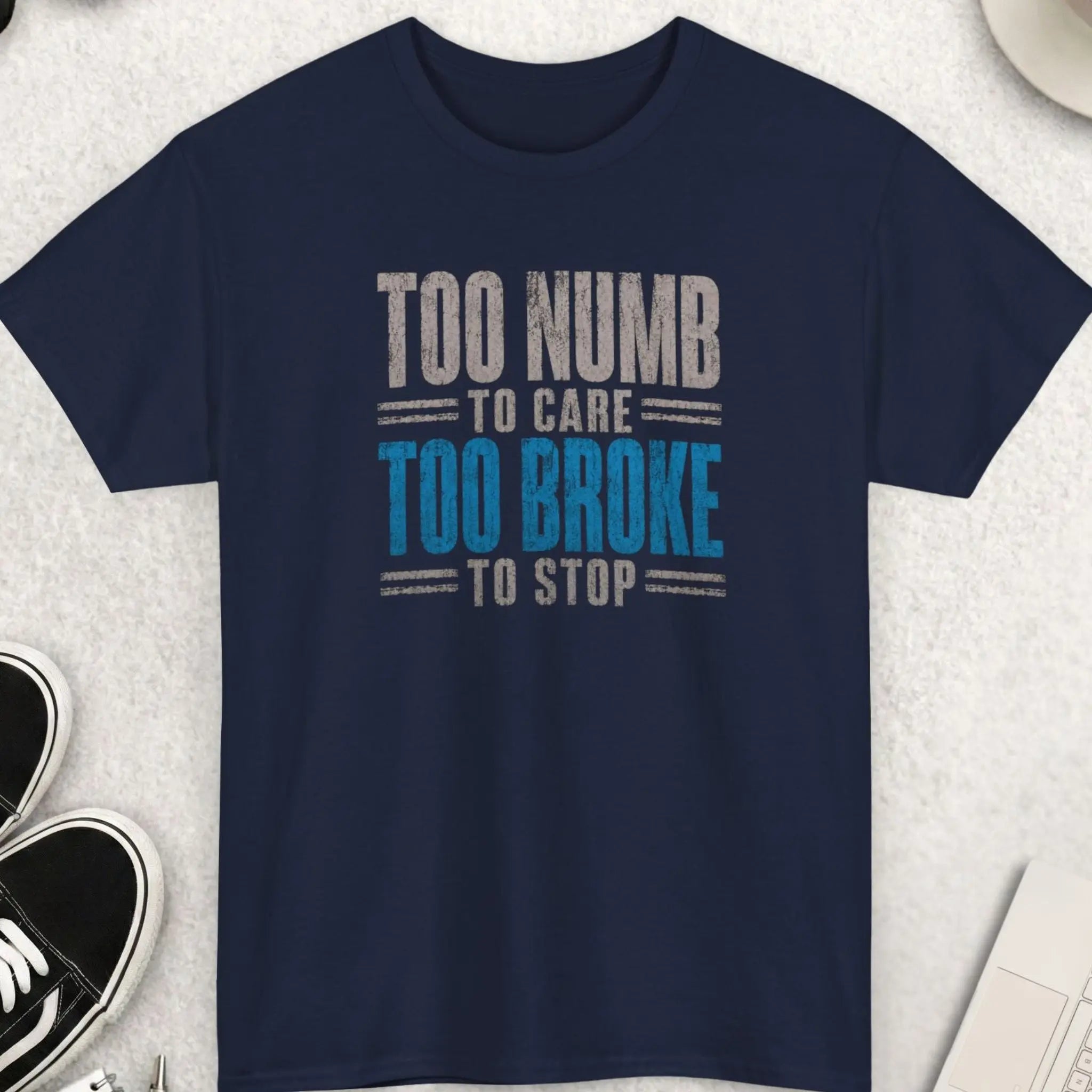 Navy blue sarcastic graphic tee with distressed cream and deep red typography reading “Too Numb To Care Too Broke To Stop” in a gritty alternative streetwear design by Mayhem Haus.