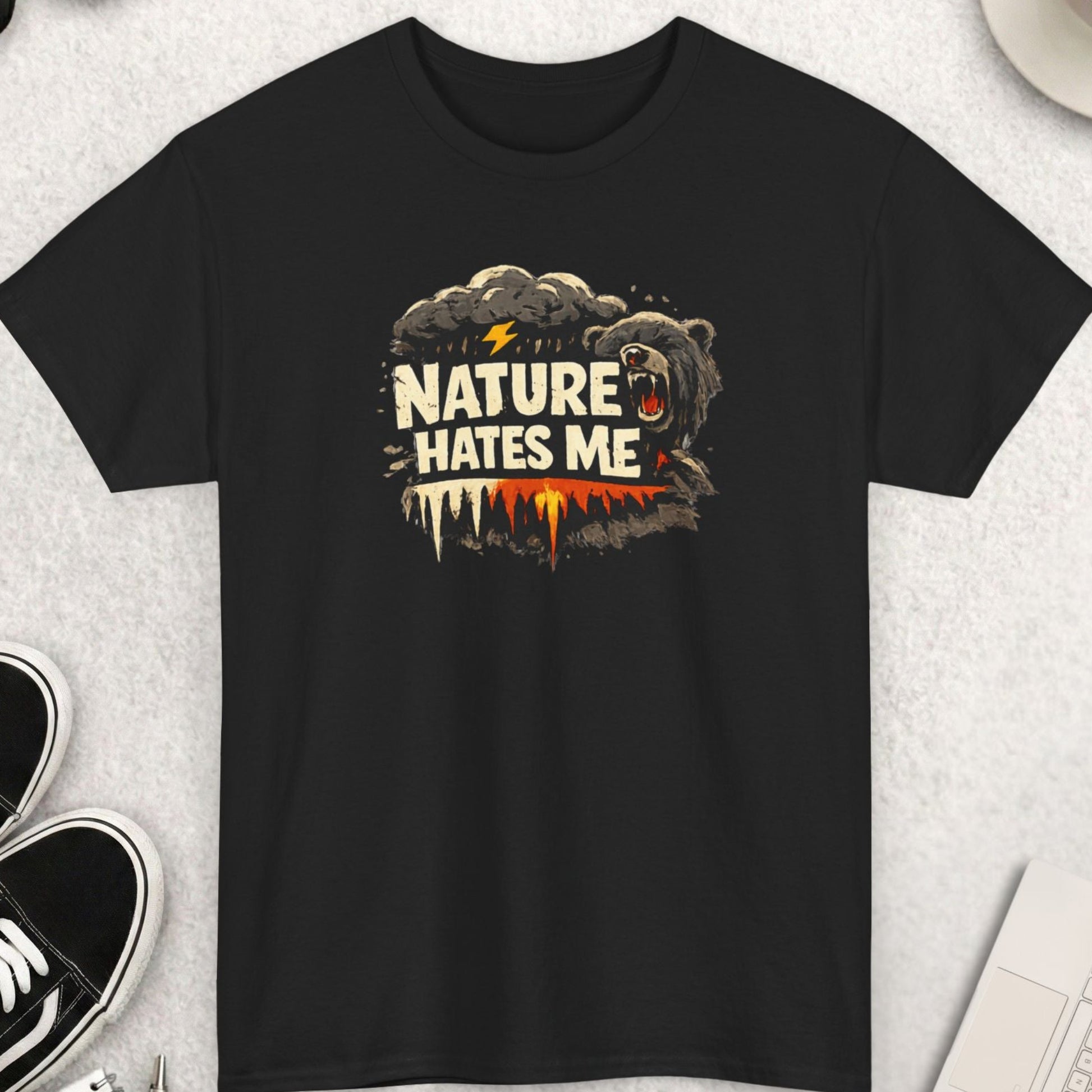 Black t-shirt with 'Nature Hates Me' graphic on a light gray surface with accessories.