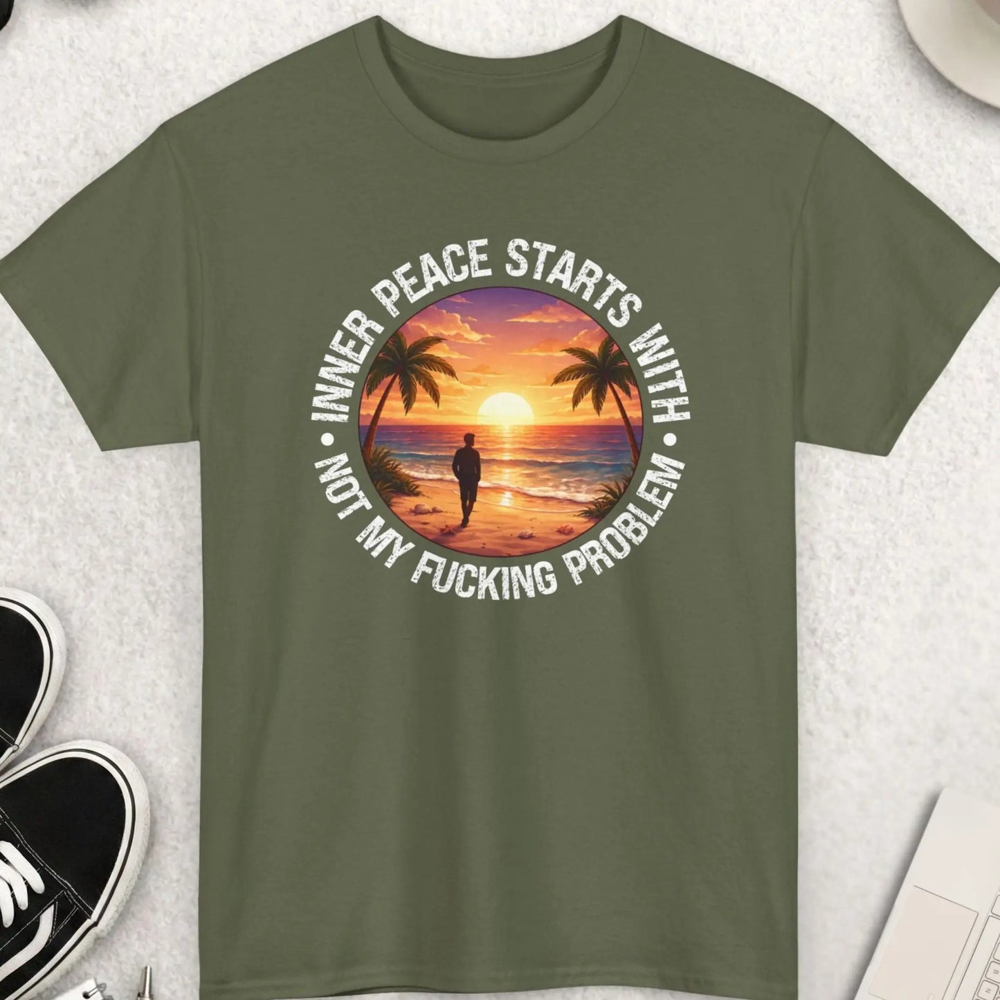 Green t-shirt with a sunset design and text on a light gray surface with accessories.