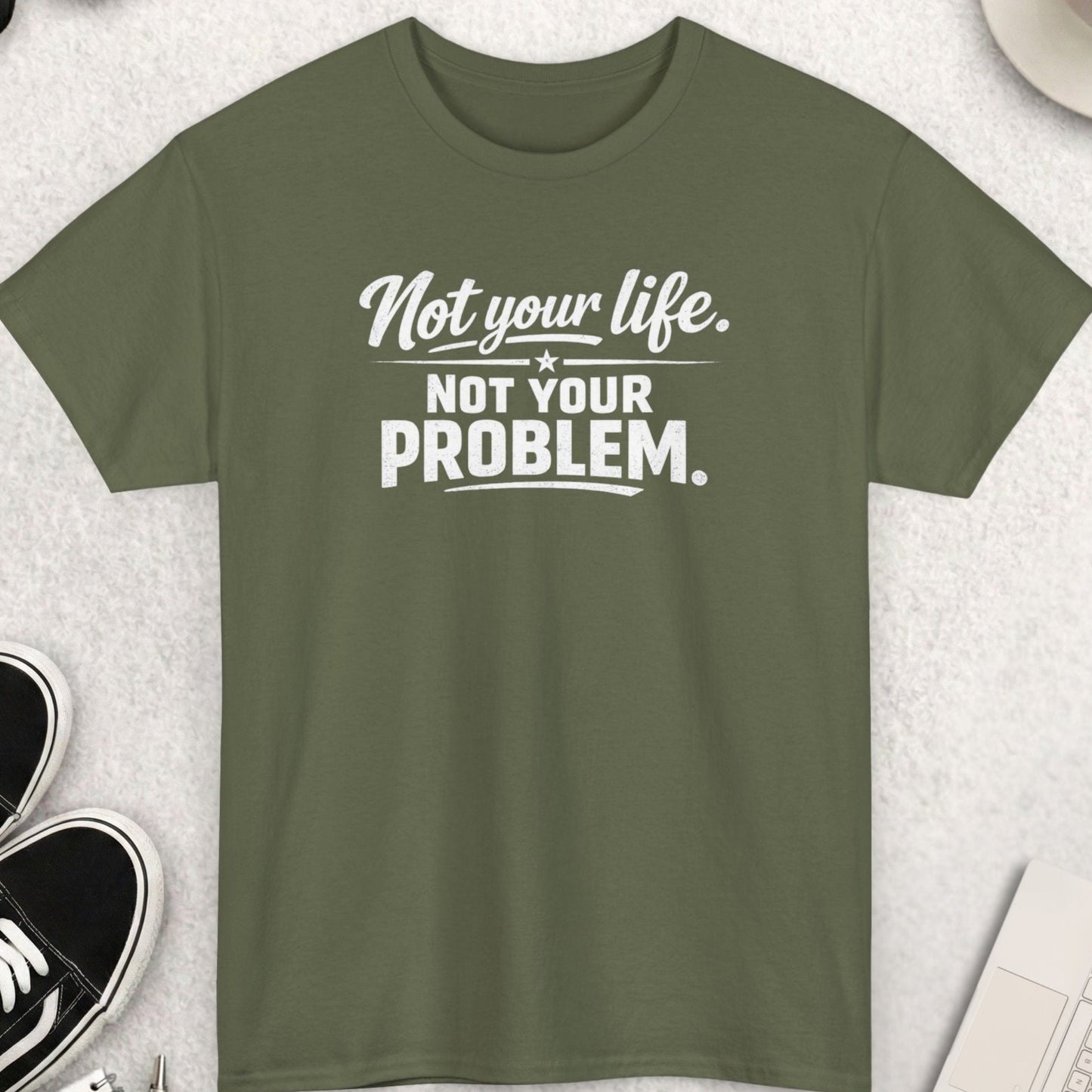 Green t-shirt with 'Not your life. Not your problem.' text on a light gray surface with shoes, coffee, and accessories.