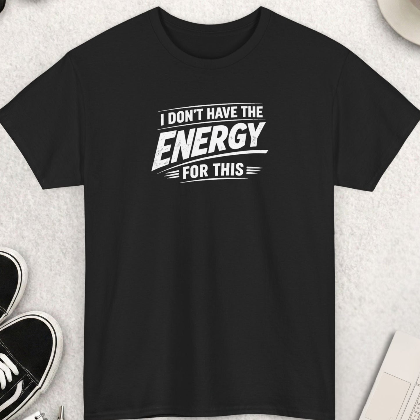 Black t-shirt with 'I don't have the energy for this' text on a light gray surface with shoes, coffee, and accessories.