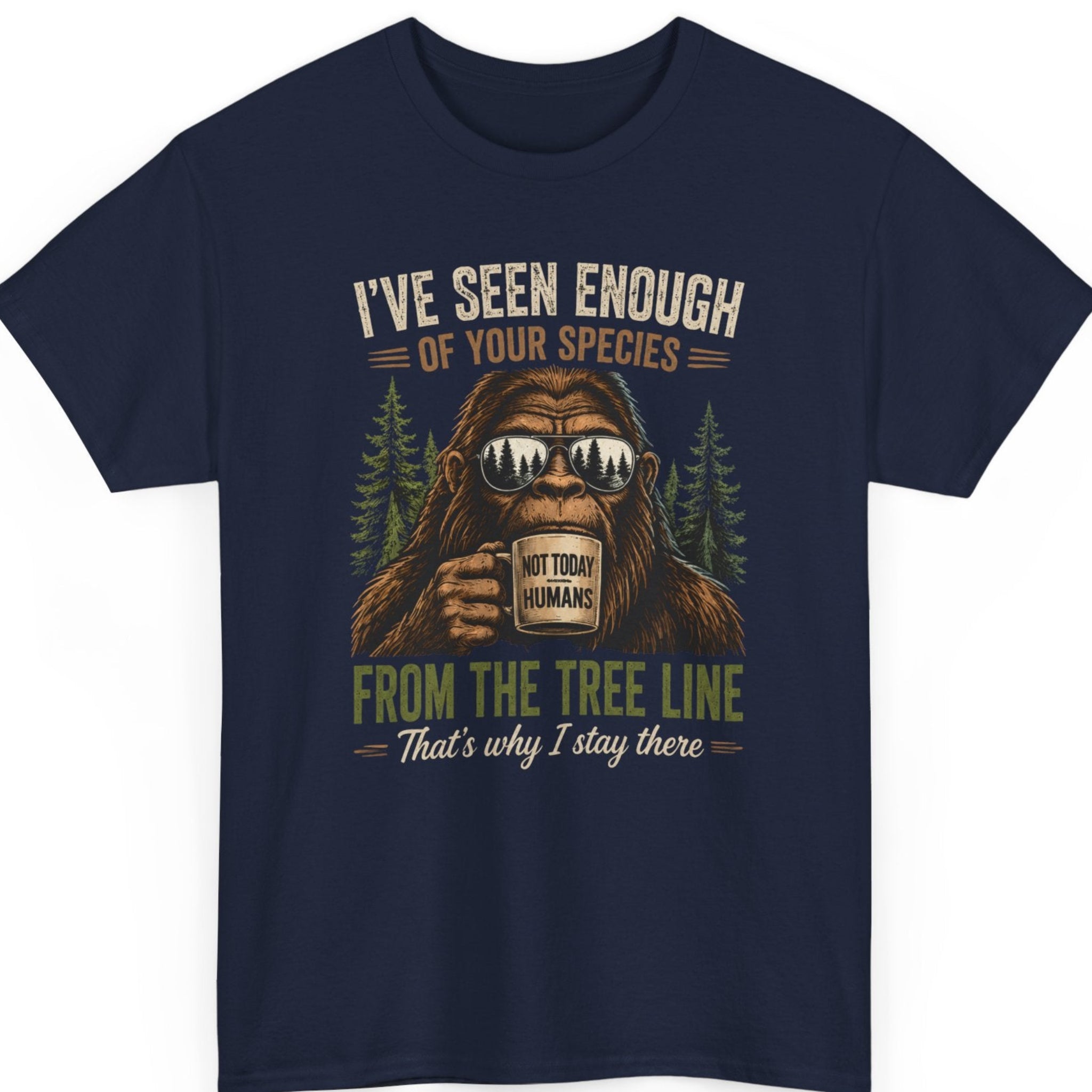 Mayhem Haus funny Bigfoot t-shirt on a navy blue shirt featuring a sarcastic Sasquatch holding a coffee mug, mirrored sunglasses reflecting a forest, evergreen trees, and the quote "I've Seen Enough Of Your Species From The Tree Line That's Why I Stay There."