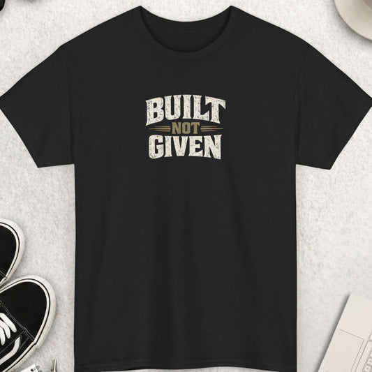 Black t-shirt with 'Built Not Given' text on a light gray surface with shoes, coffee, and accessories.