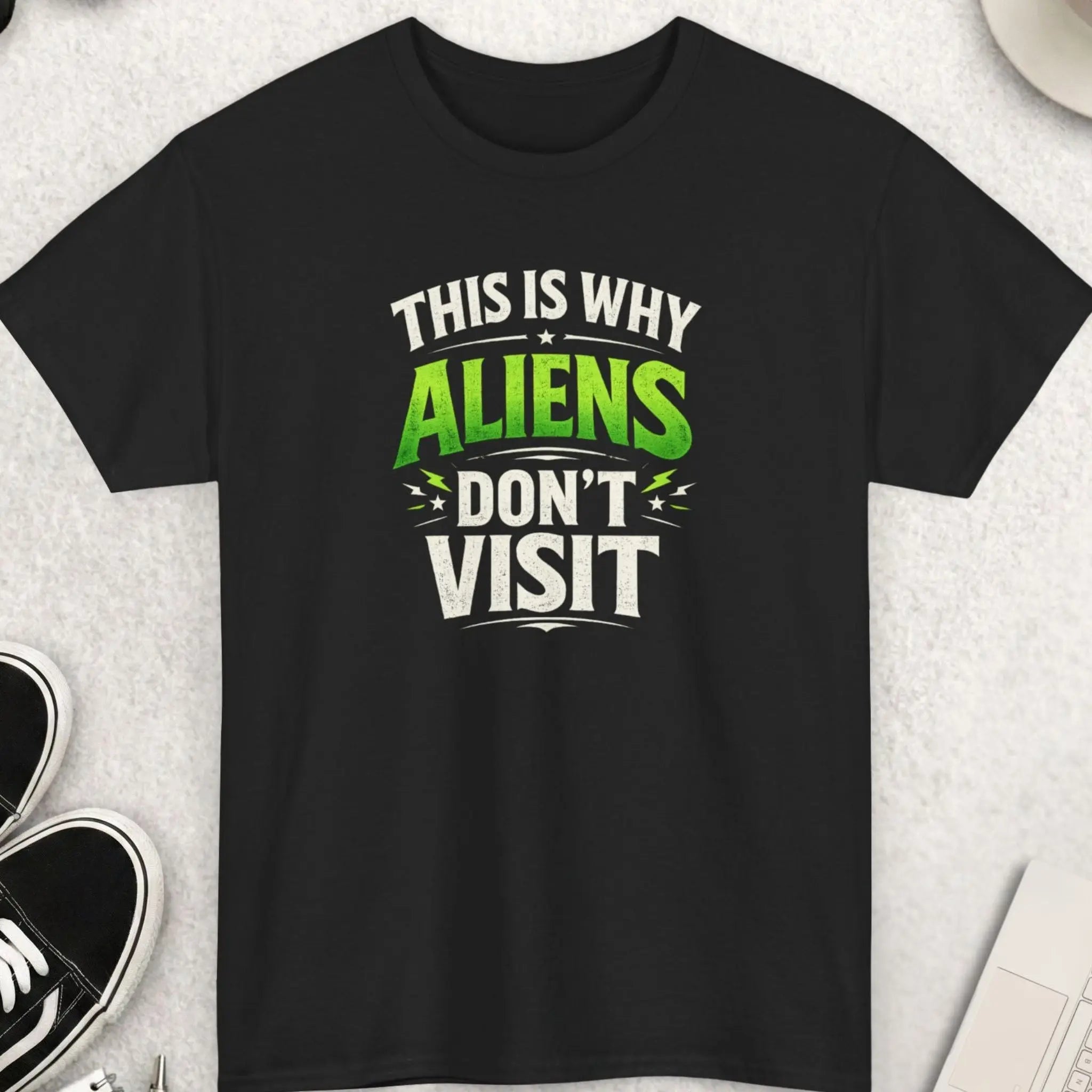 Black t-shirt with humorous text design on a light gray surface with accessories.