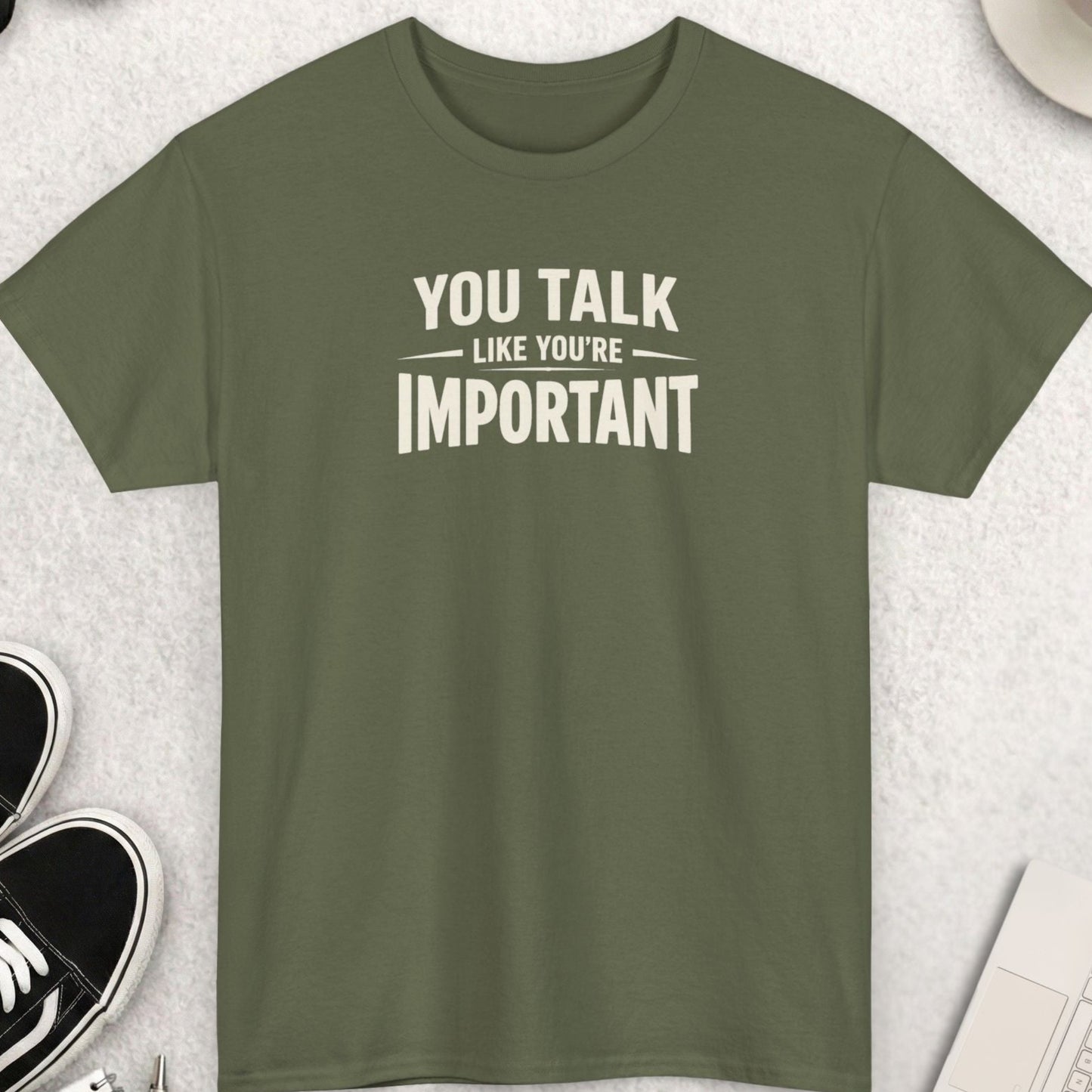 Green t-shirt with 'You talk like you're important' text on a light gray surface with accessories.