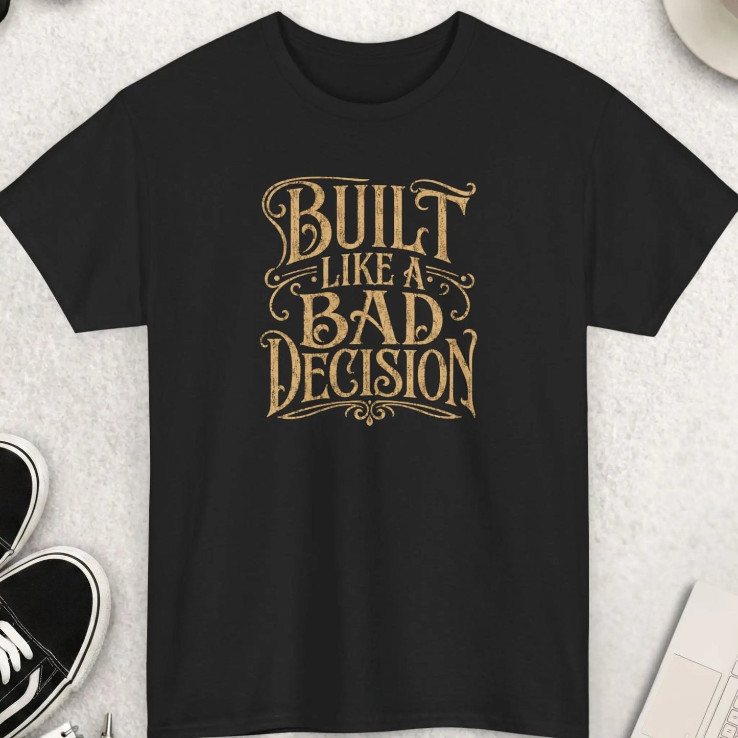 Distressed vintage western typography graphic t-shirt in black featuring the phrase “Built Like A Bad Decision” in large retro cream lettering with worn texture and bold outlaw-inspired styling.