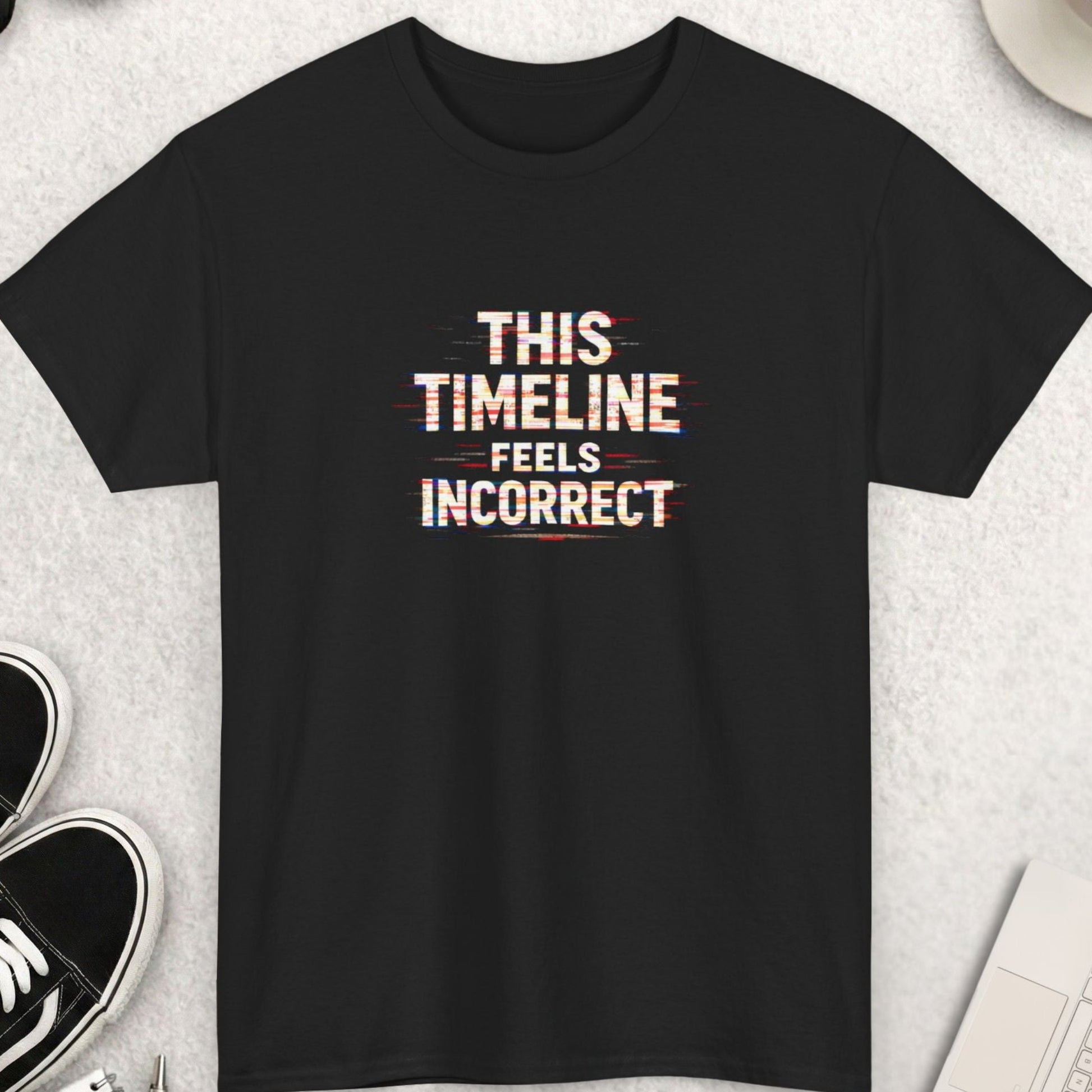 Black t-shirt with 'THIS TIMELINE FEELS Incorrect' text on a light gray surface with shoes, coffee, and accessories.