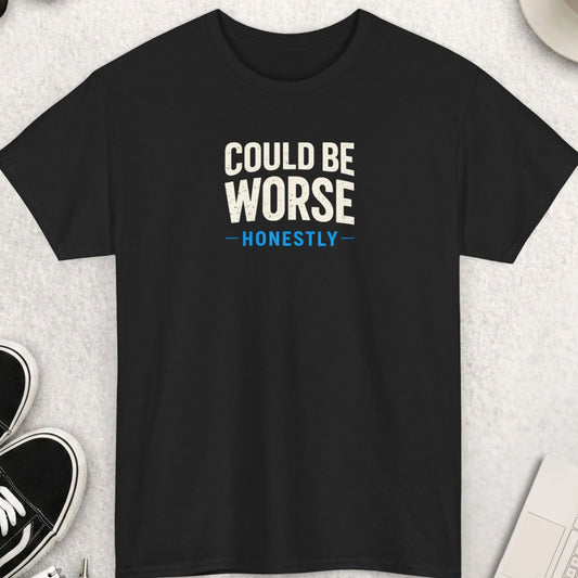 Black t-shirt with 'Could Be Worse Honestly' text on a light gray surface with shoes, coffee, and accessories.