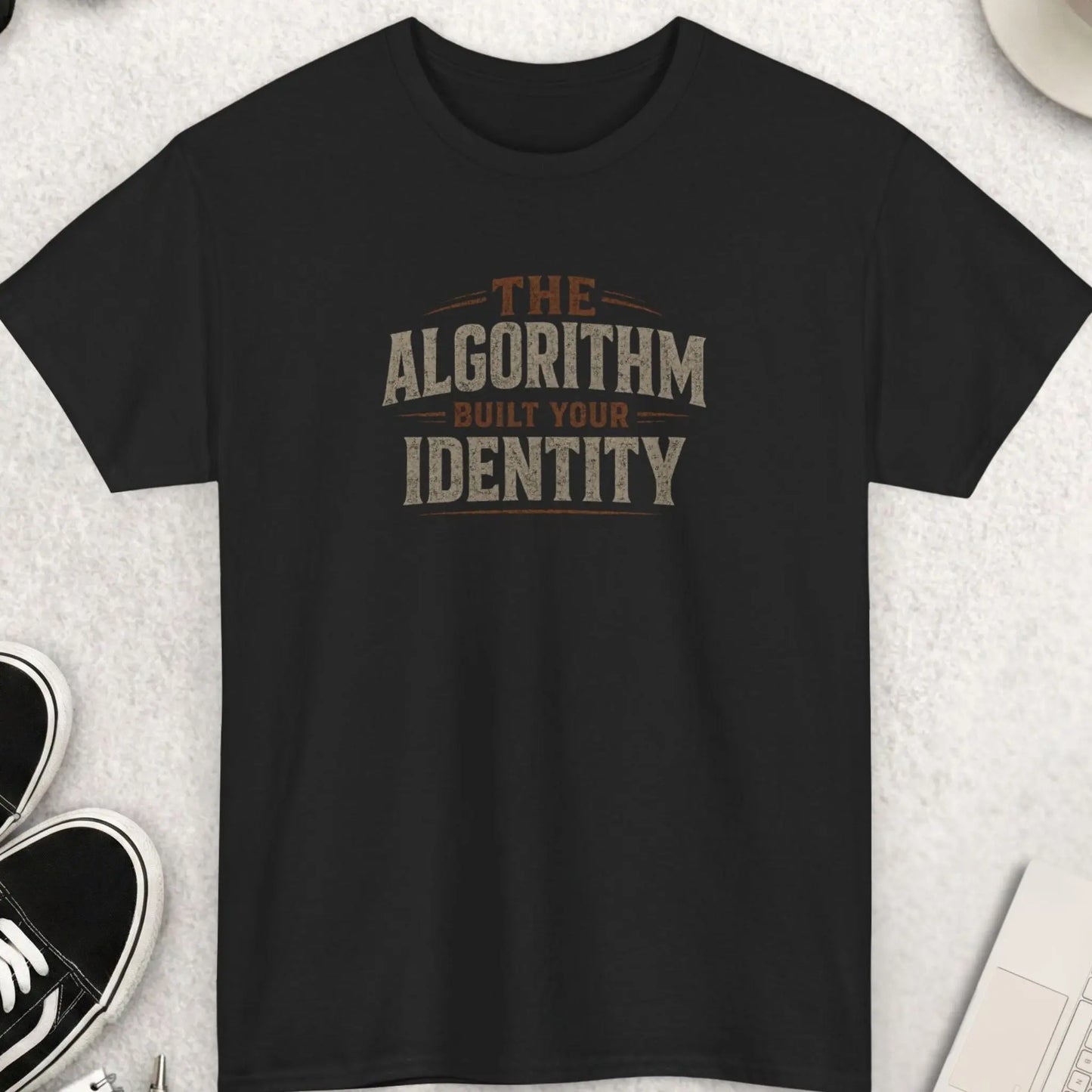 Black t-shirt featuring distressed vintage typography reading “The Algorithm Built Your Identity” in muted earth-tone colors with a bold minimalist layout.