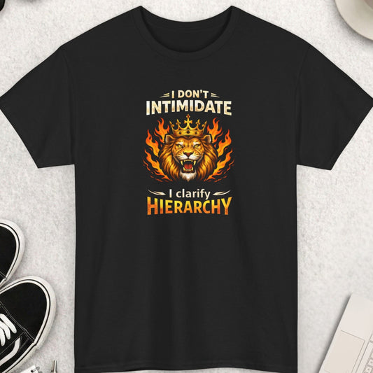 Black t-shirt ' I Don’t Intimidate – I Clarify Hierarchy' on a light gray surface with shoes, coffee, and accessories.