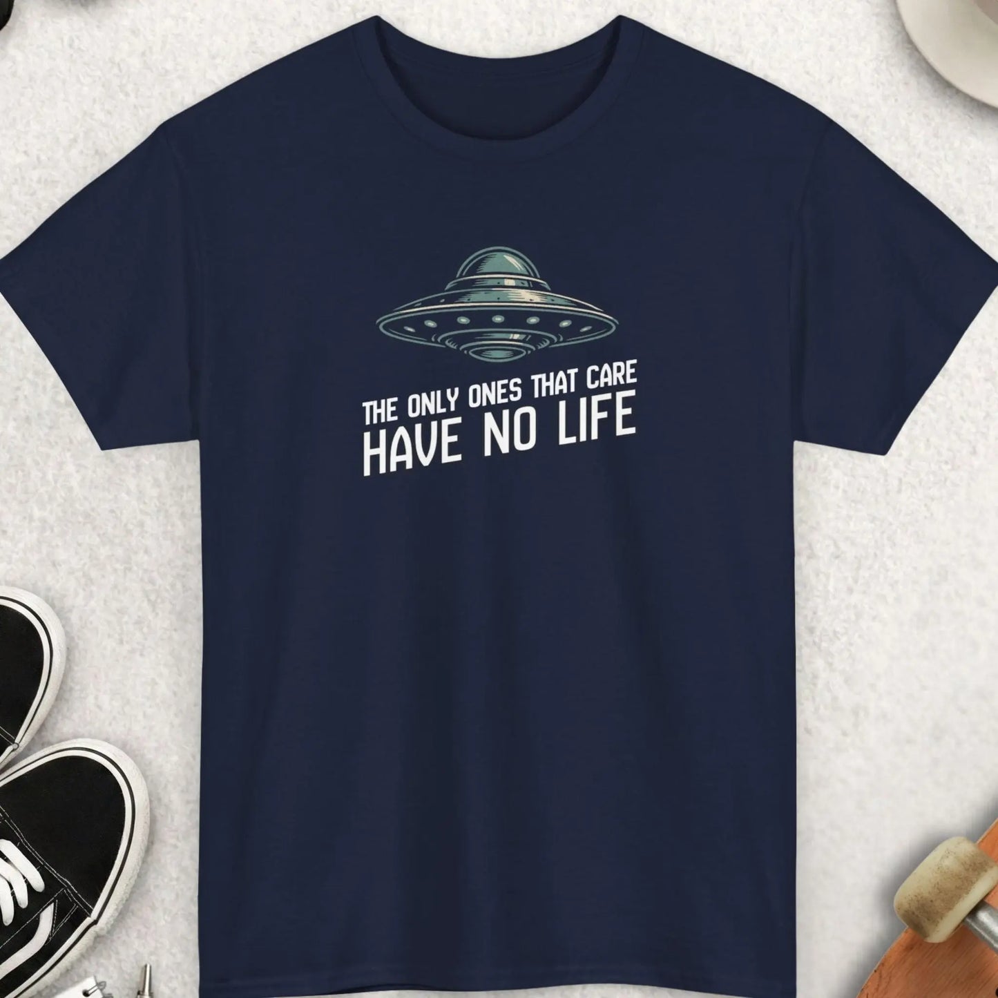Navy blue "The Only Ones That Care Have No Life" t-shirt with UFO graphic and text on a light gray surface with accessories.