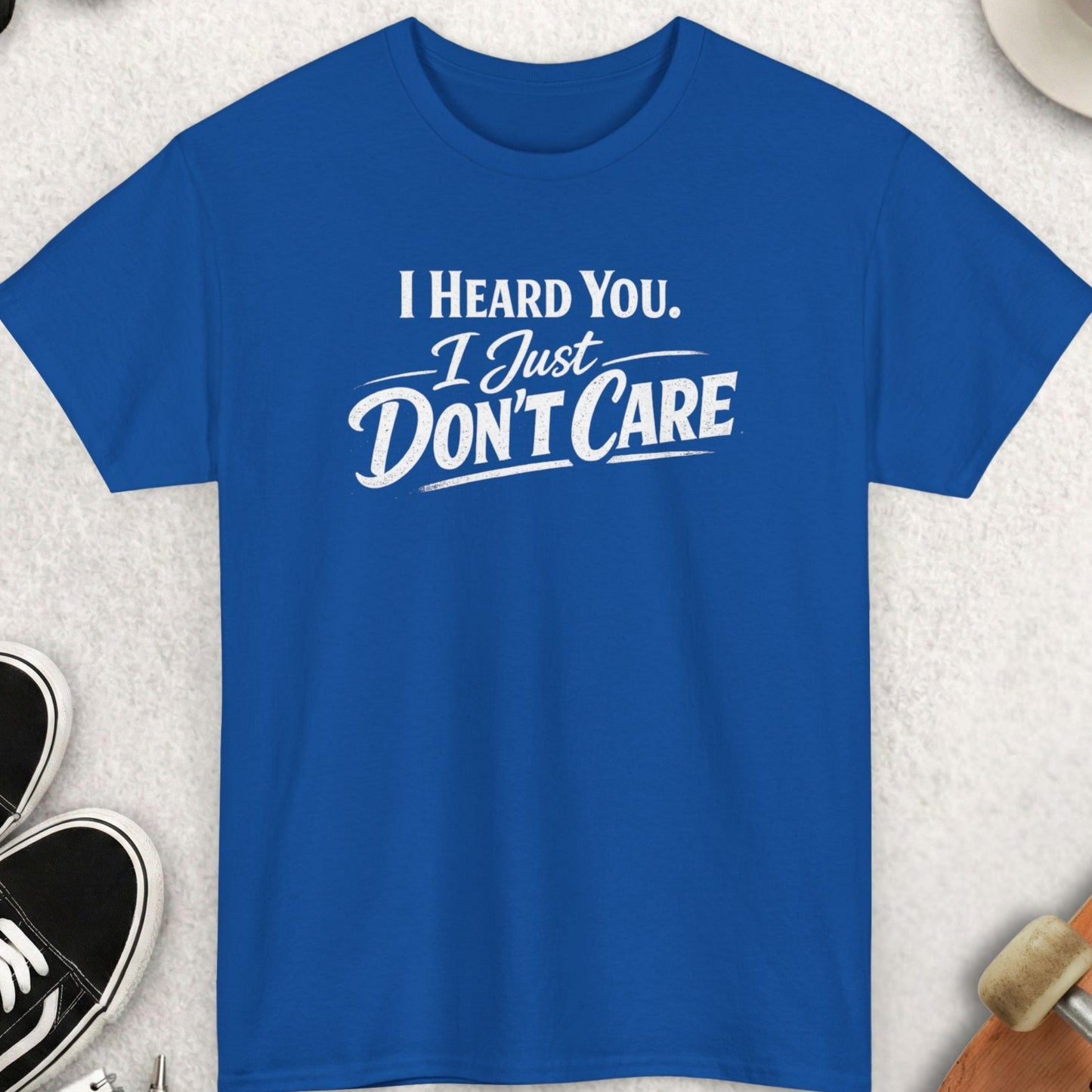 Blue t-shirt with 'I Heard You, I Just Don't Care' text on a light gray surface with accessories.