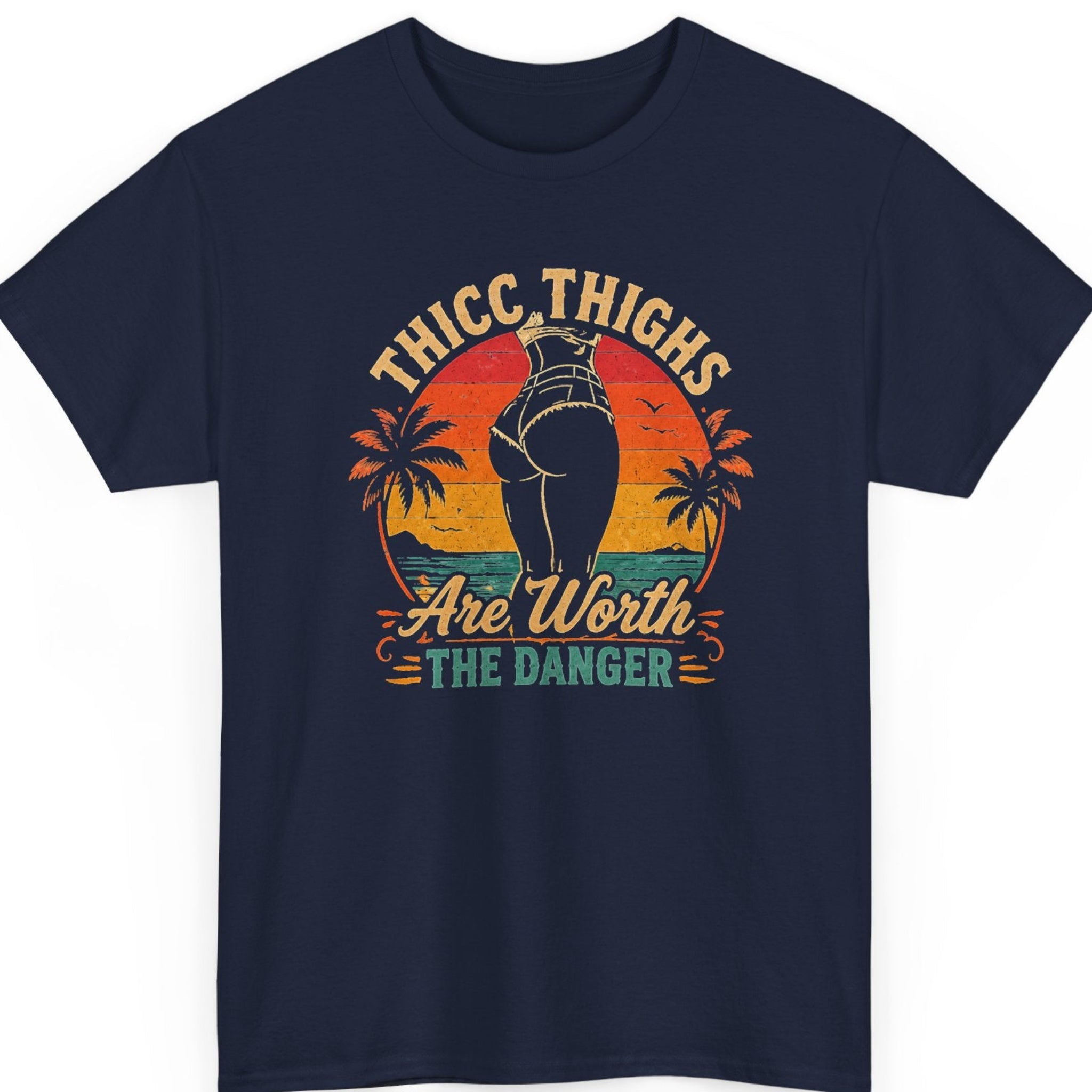 Mayhem Haus cheeky statement shirt on a navy blue t-shirt featuring a retro beach-inspired design with sunset colors, tropical scenery, and the playful phrase “Thicc Thighs Are Worth the Danger.”