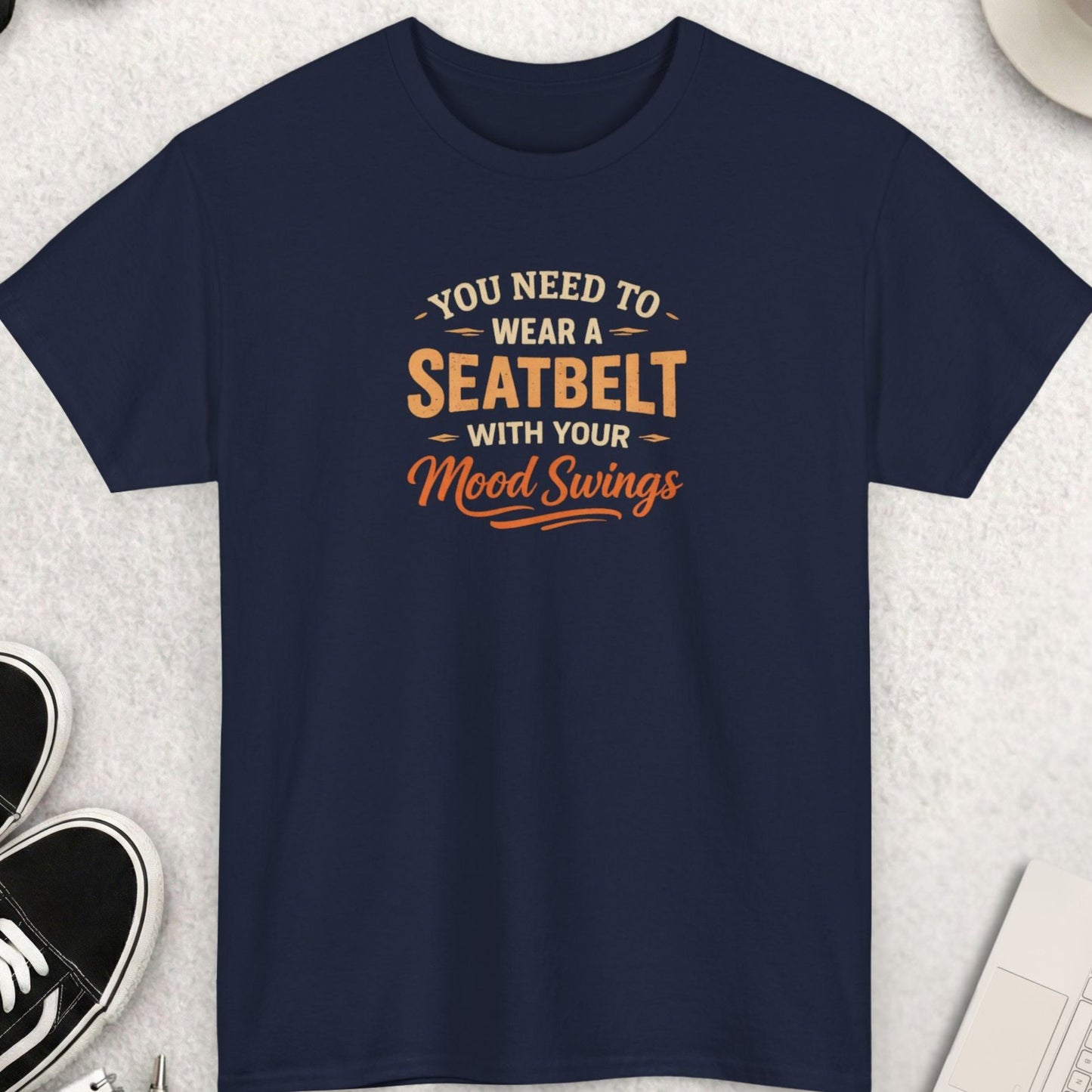 Navy blue t-shirt with humorous text design on a light gray surface with accessories.