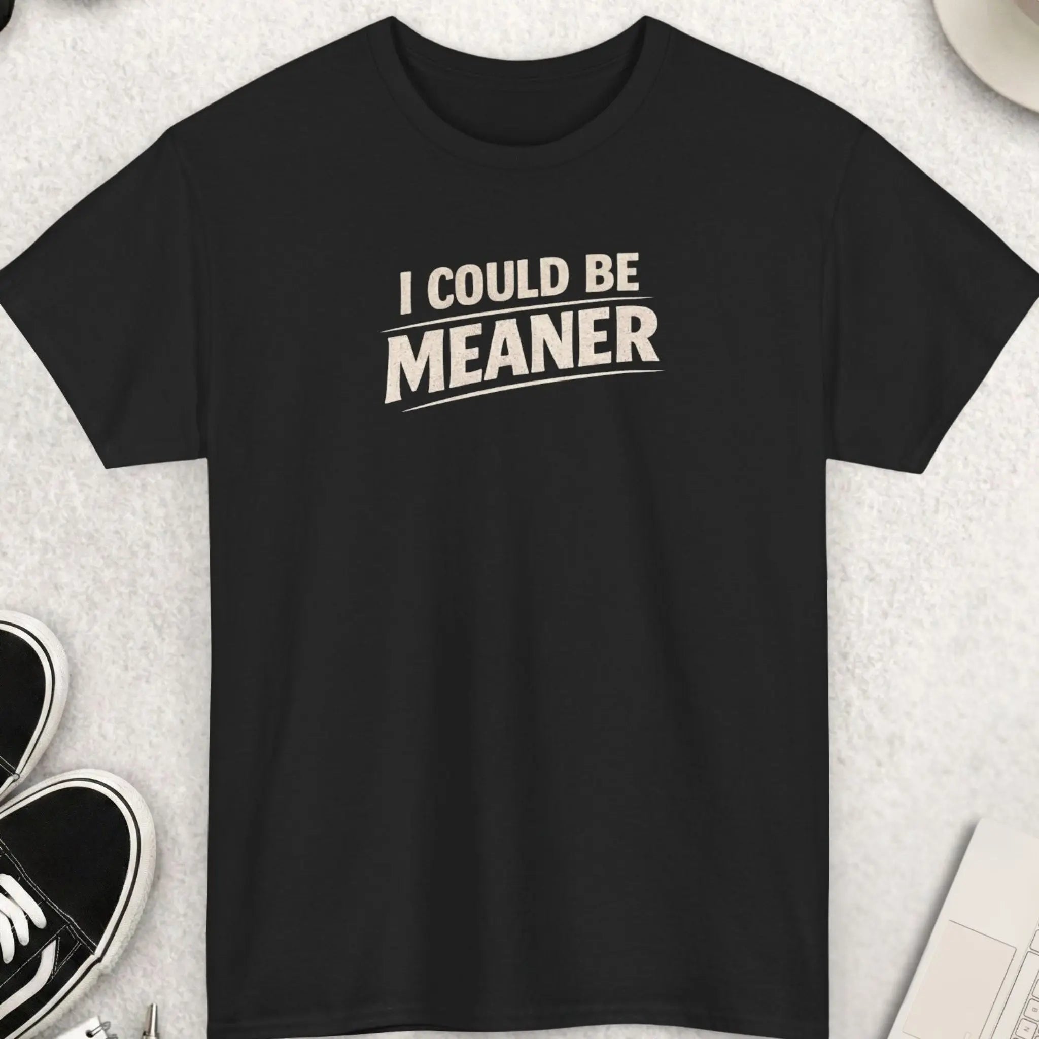 Black t-shirt with 'I Could Be Meaner' text on a light gray surface with shoes, coffee, and accessories.