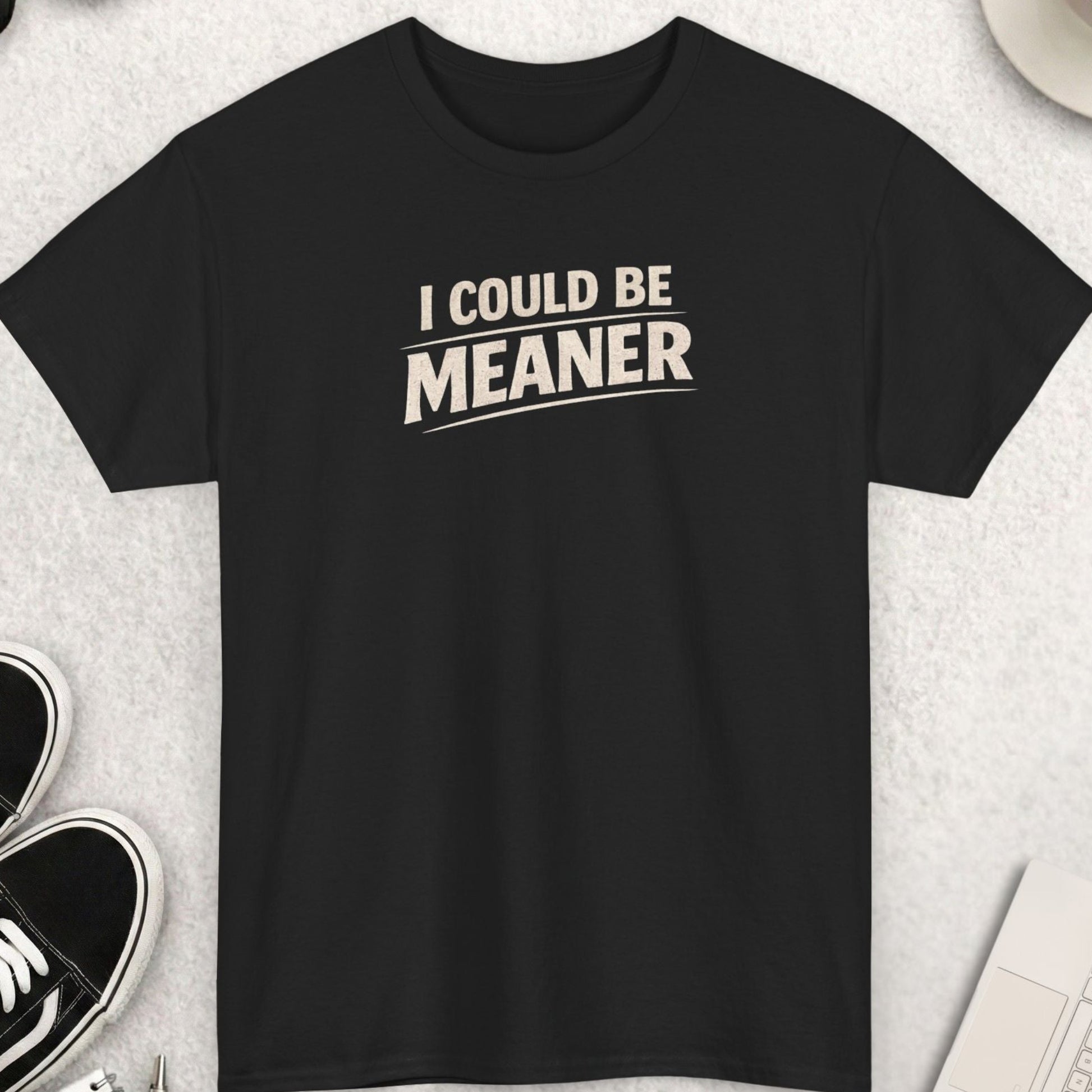 Black t-shirt with 'I Could Be Meaner' text on a light gray surface with shoes, coffee, and accessories.
