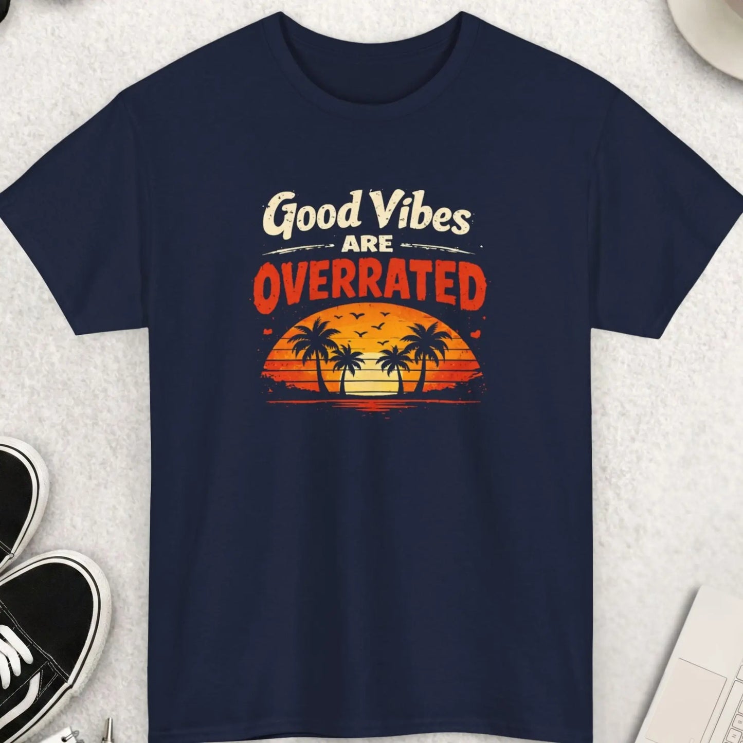 Navy blue t-shirt with 'Good Vibes Are Overrated' graphic on a light gray surface with accessories.