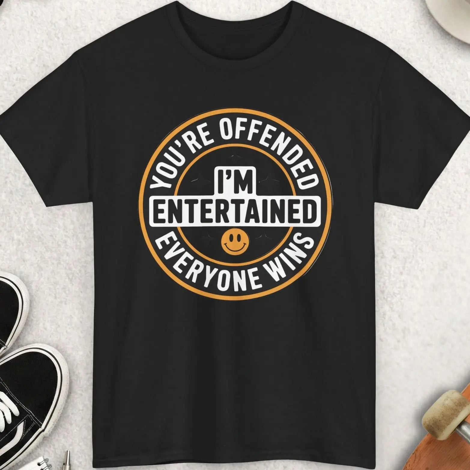 Black t-shirt with humorous graphic design on a light gray surface with accessories.