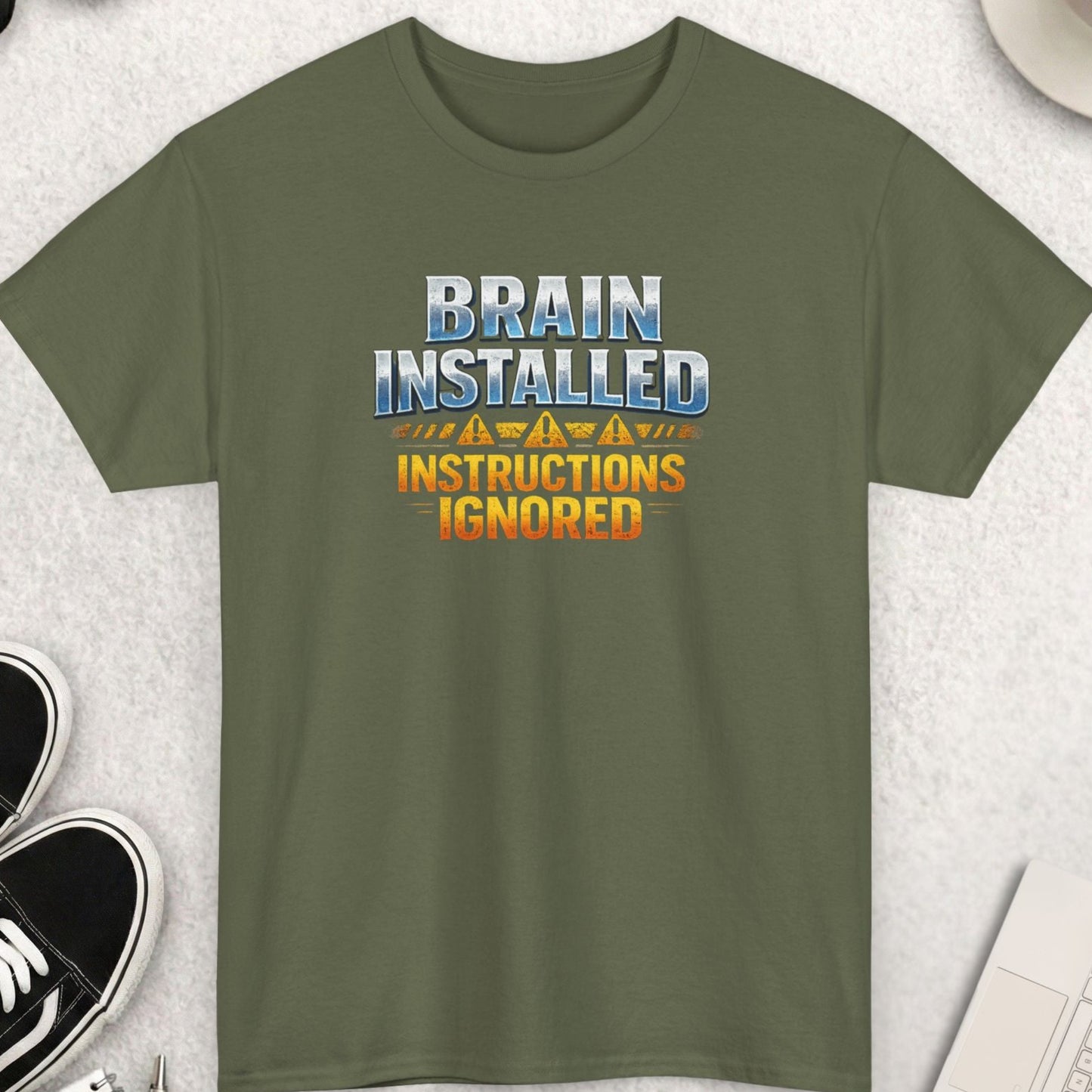 Green t-shirt with humorous text design on a light gray surface with accessories.