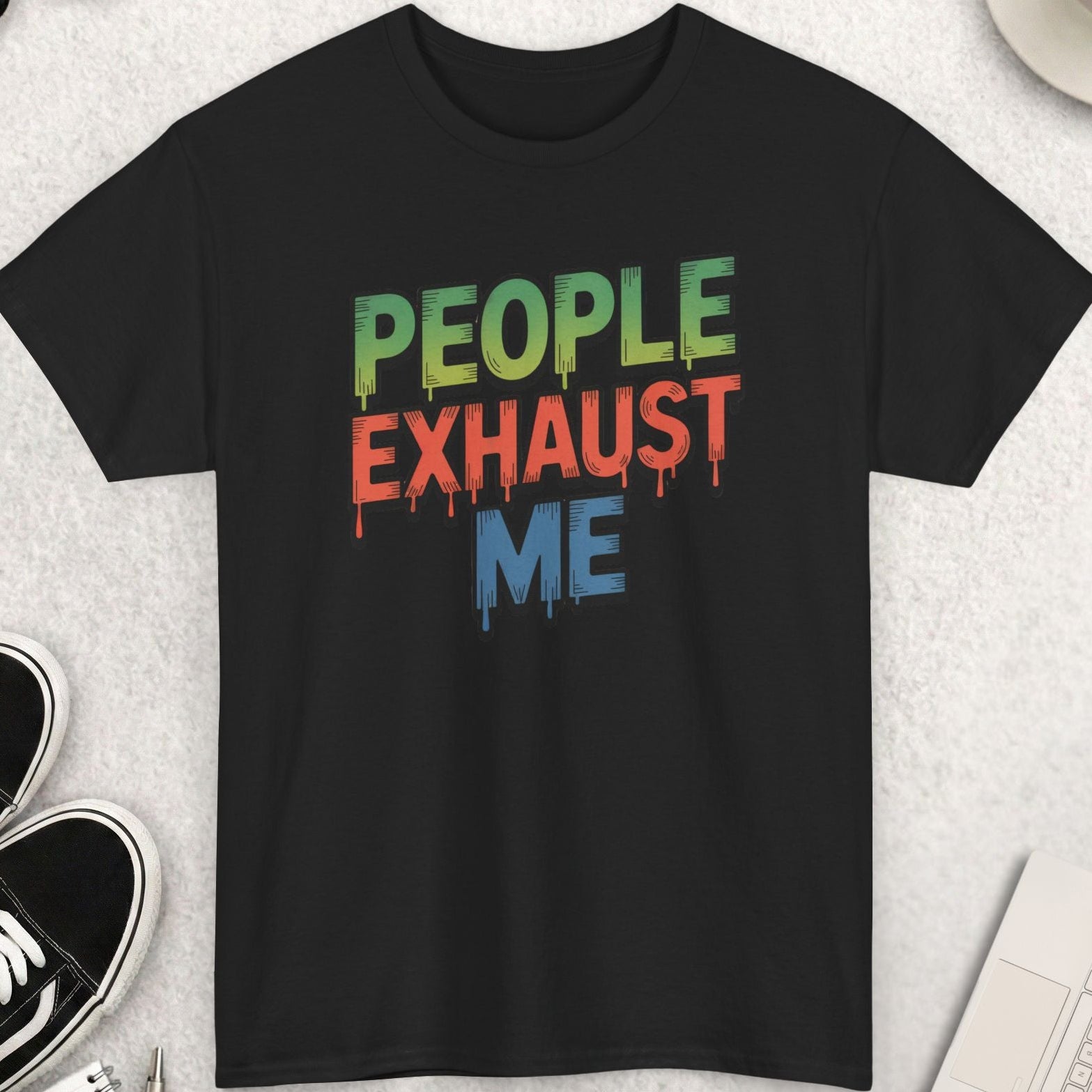 Black t-shirt with 'People Exhaust Me' text on a light gray surface with accessories.