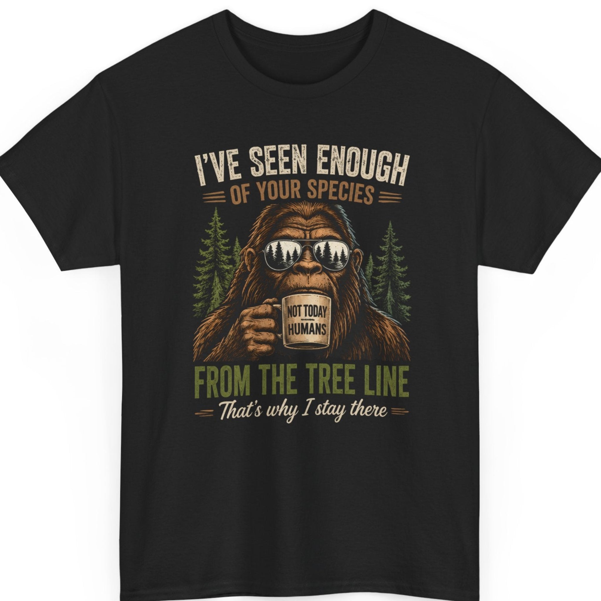 Mayhem Haus Bigfoot graphic t-shirt on a black shirt featuring a grumpy Sasquatch wearing reflective sunglasses and drinking from a mug labeled "Not Today Humans," surrounded by pine trees with the phrase "I've Seen Enough Of Your Species From The Tree Line That's Why I Stay There" in distressed outdoor typography.