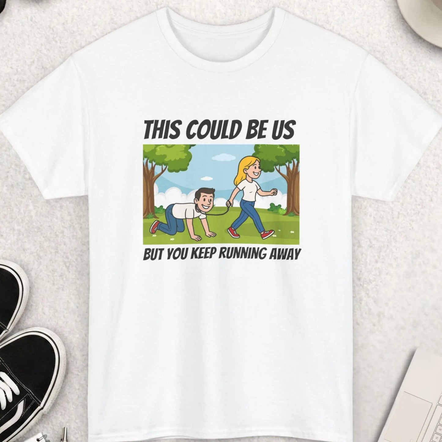 White t-shirt with a graphic and text on a light gray surface with accessories around.