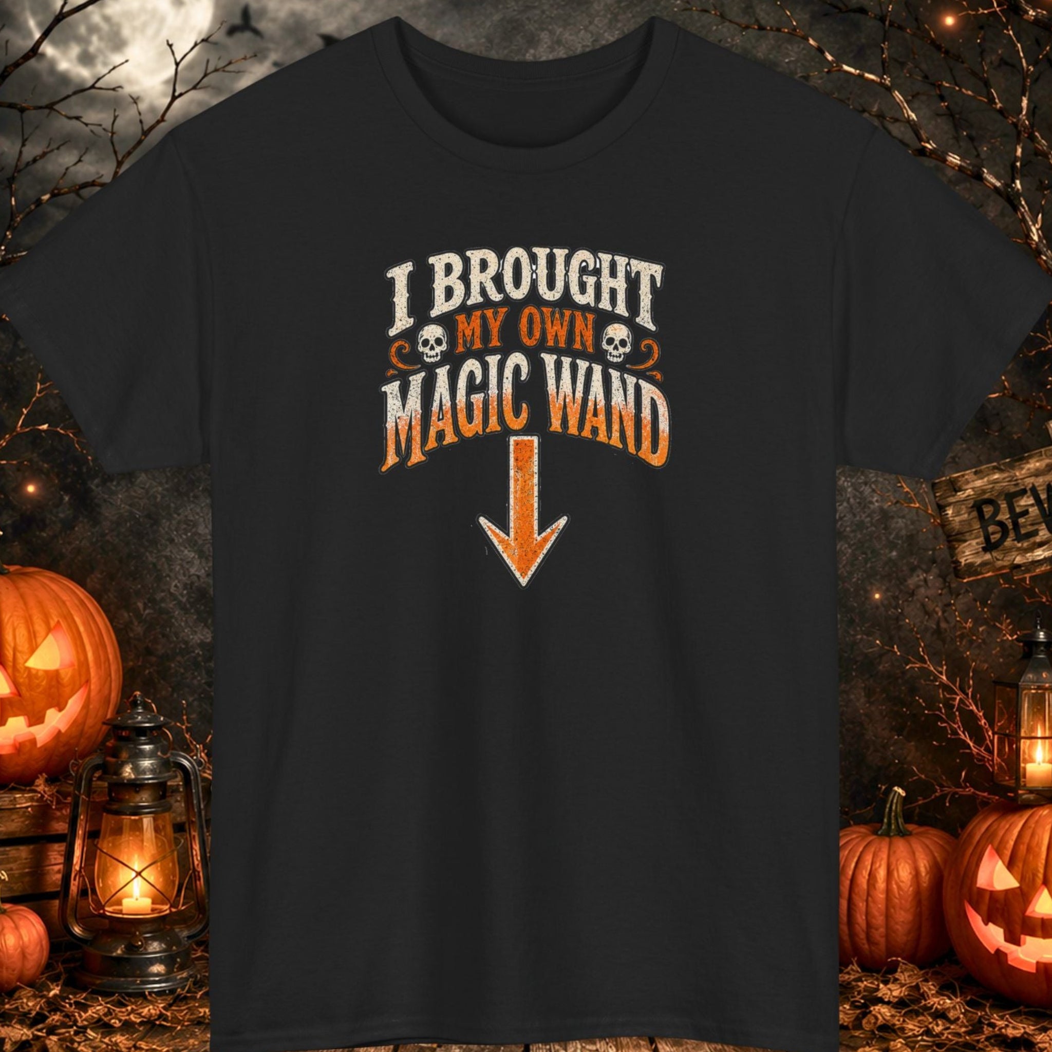 Mayhem Haus black Halloween T-shirt featuring the phrase "I Brought My Own Magic Wand" in distressed orange and cream typography with skull accents and a large downward-pointing arrow. The minimalist design combines vintage Halloween aesthetics with playful adult humor.