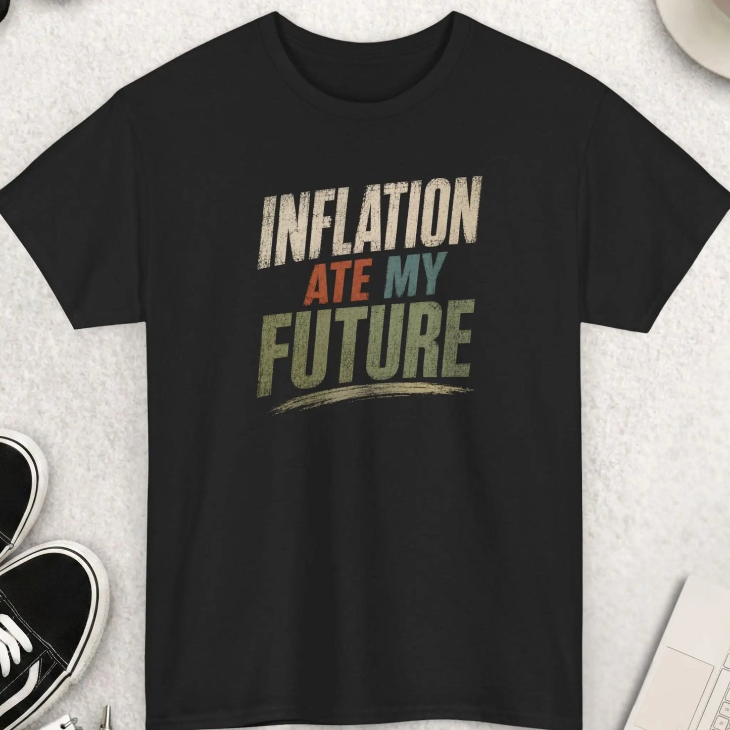 Black t-shirt featuring distressed bold typography reading “Inflation Ate My Future” in muted earth-tone colors with a minimalist statement design.